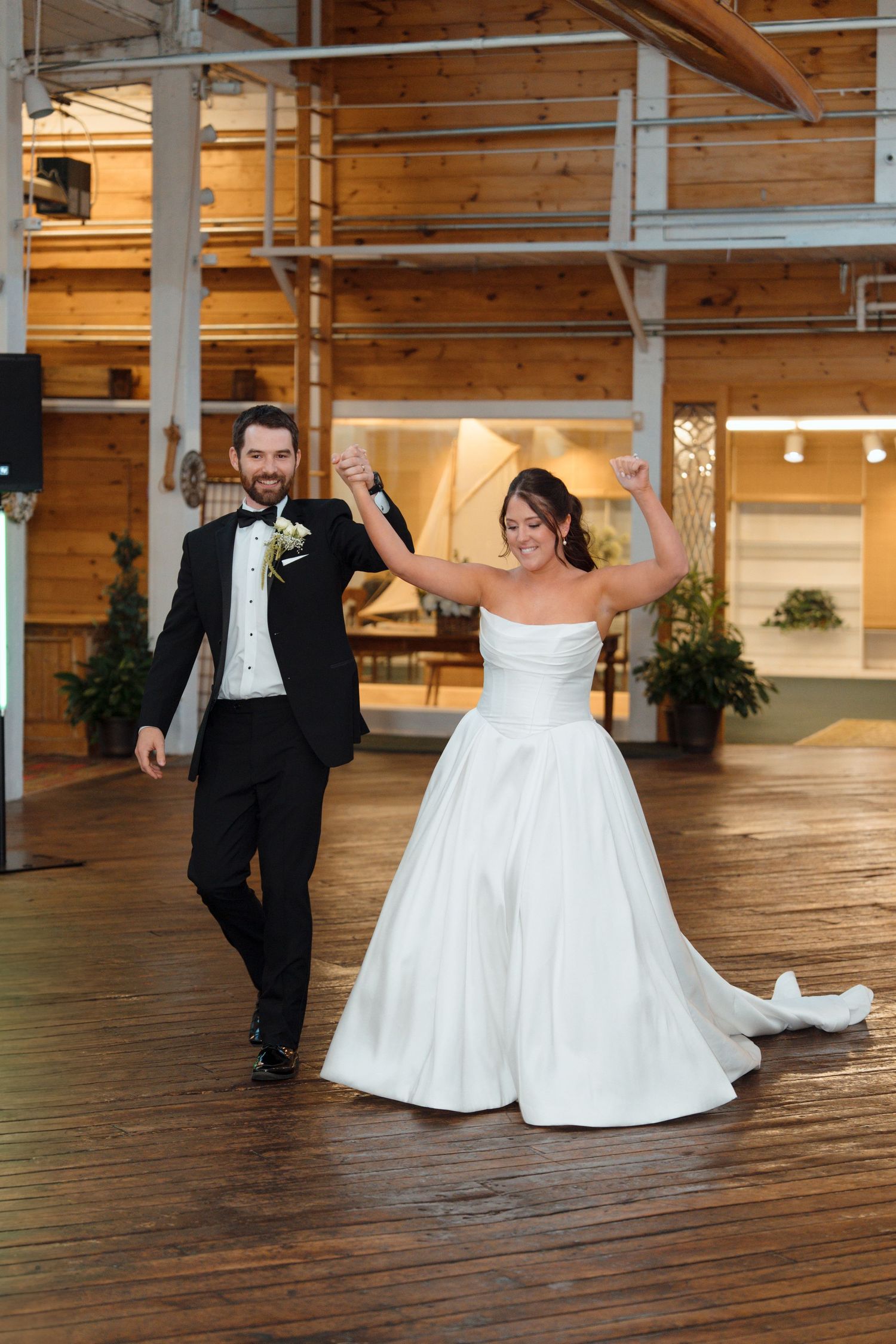 Bride and groom celebrate their grand entrance on a wooden dance floor in a rustic wedding venue.