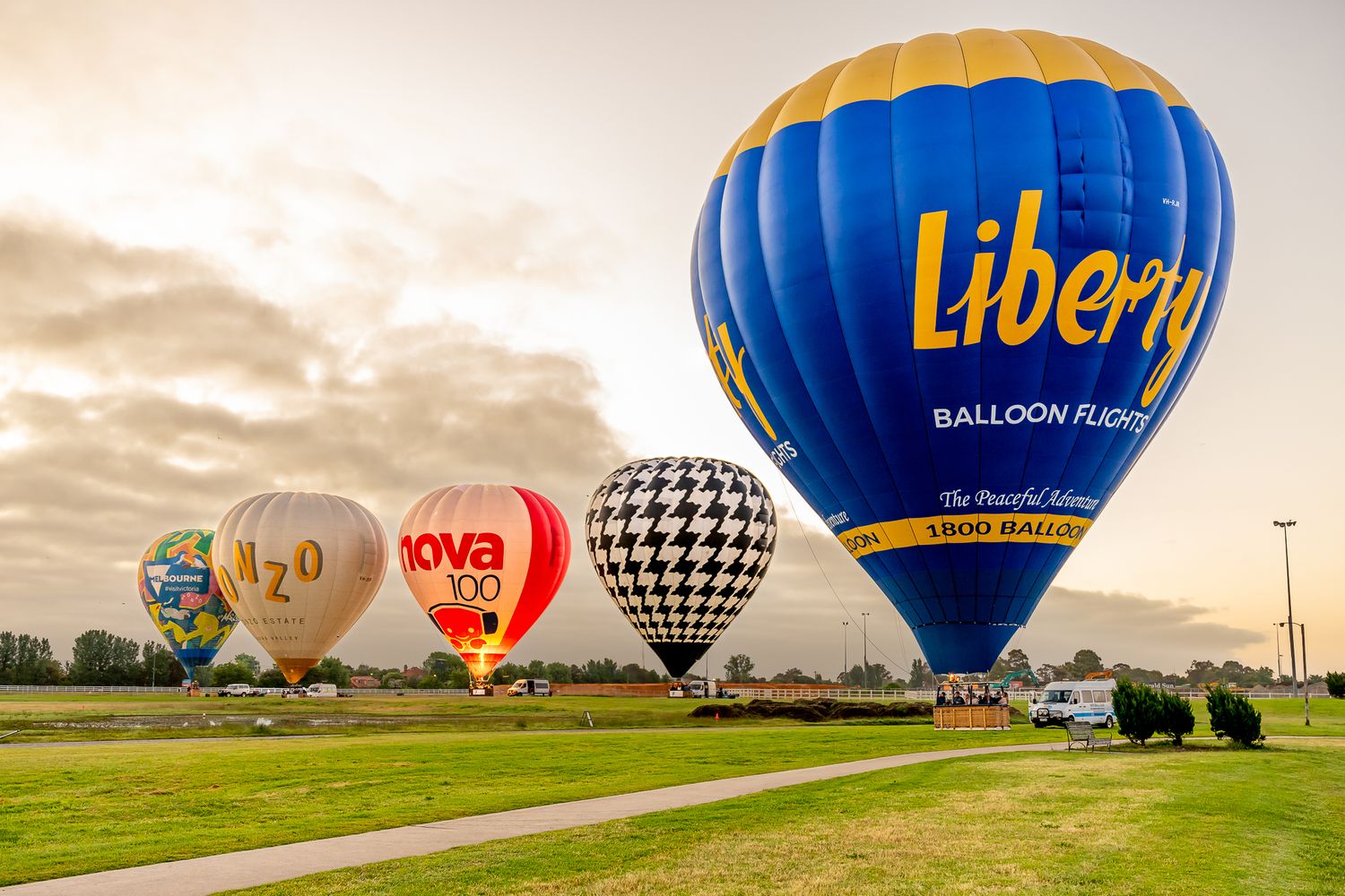 Colorful hot air balloons including Liberty Balloon Flights inflating on a green field at dusk.