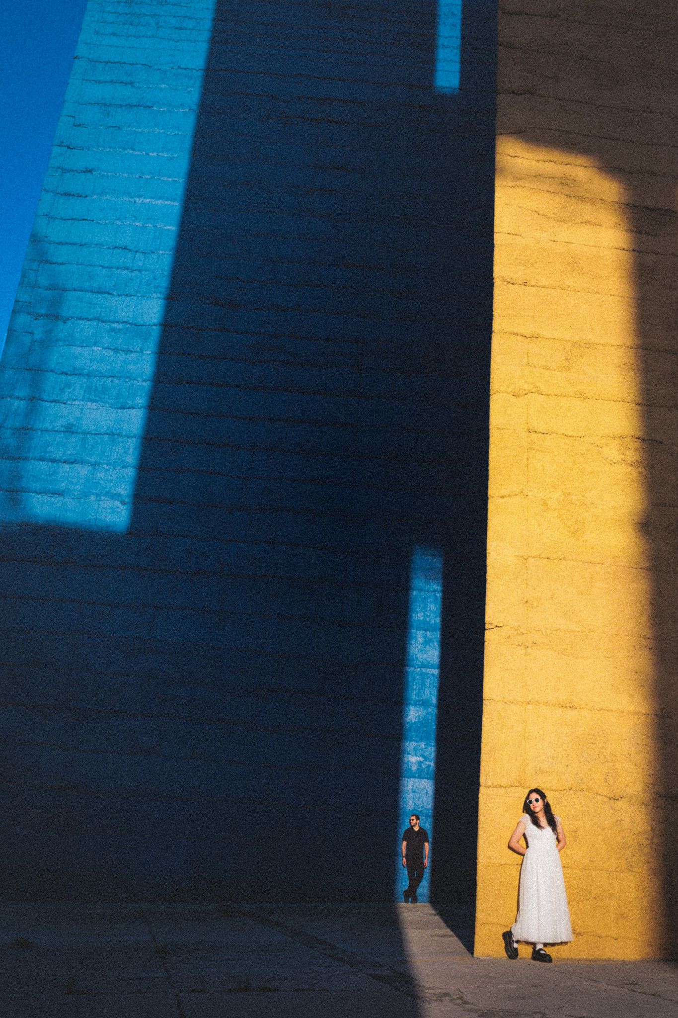 Couple stands between towering stone walls bathed in golden and blue light, creating dramatic contrast.