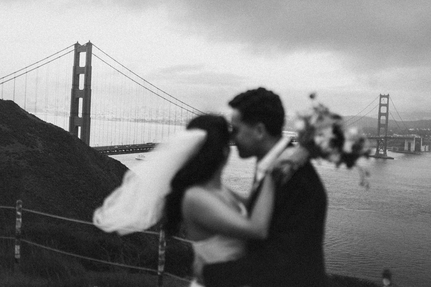 Black and white photo of a couple kissing with the Golden Gate Bridge in the background on their wedding day.