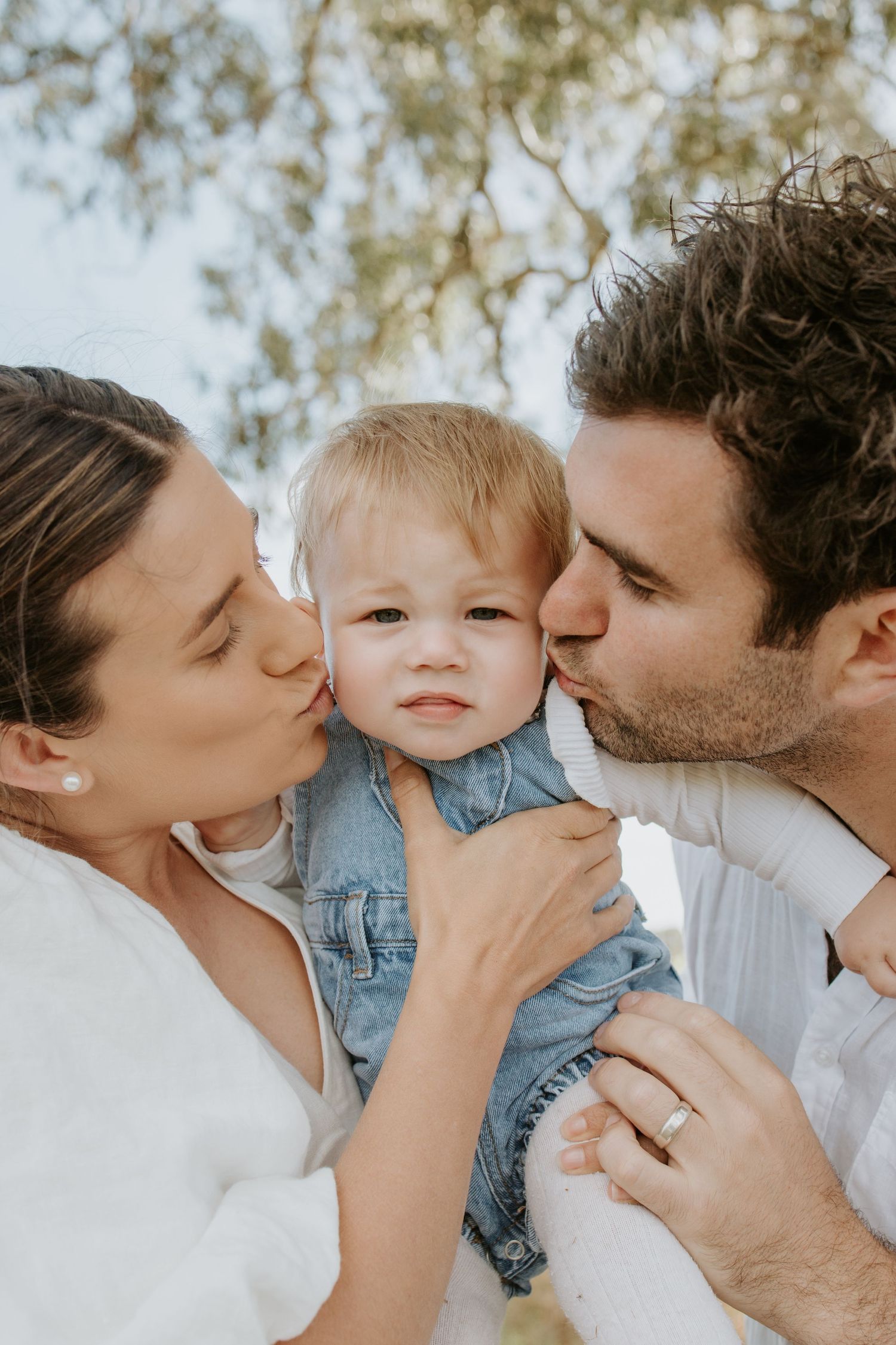 Mother and father kissing their daughter beneath a tree — Adelaide family photography with heartfelt connection.