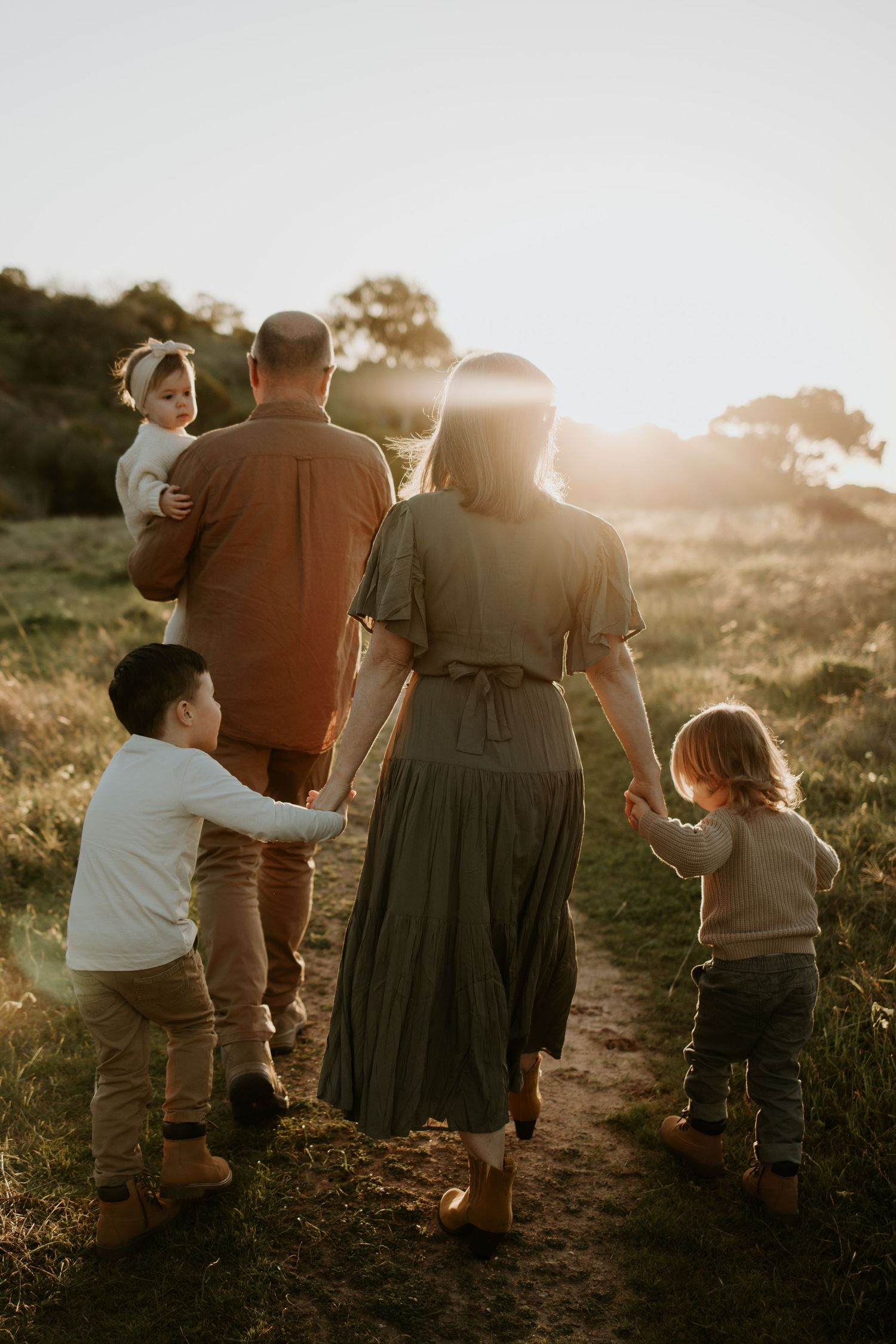 Family walking through sunlit field at sunset — natural outdoor family photography in Adelaide.