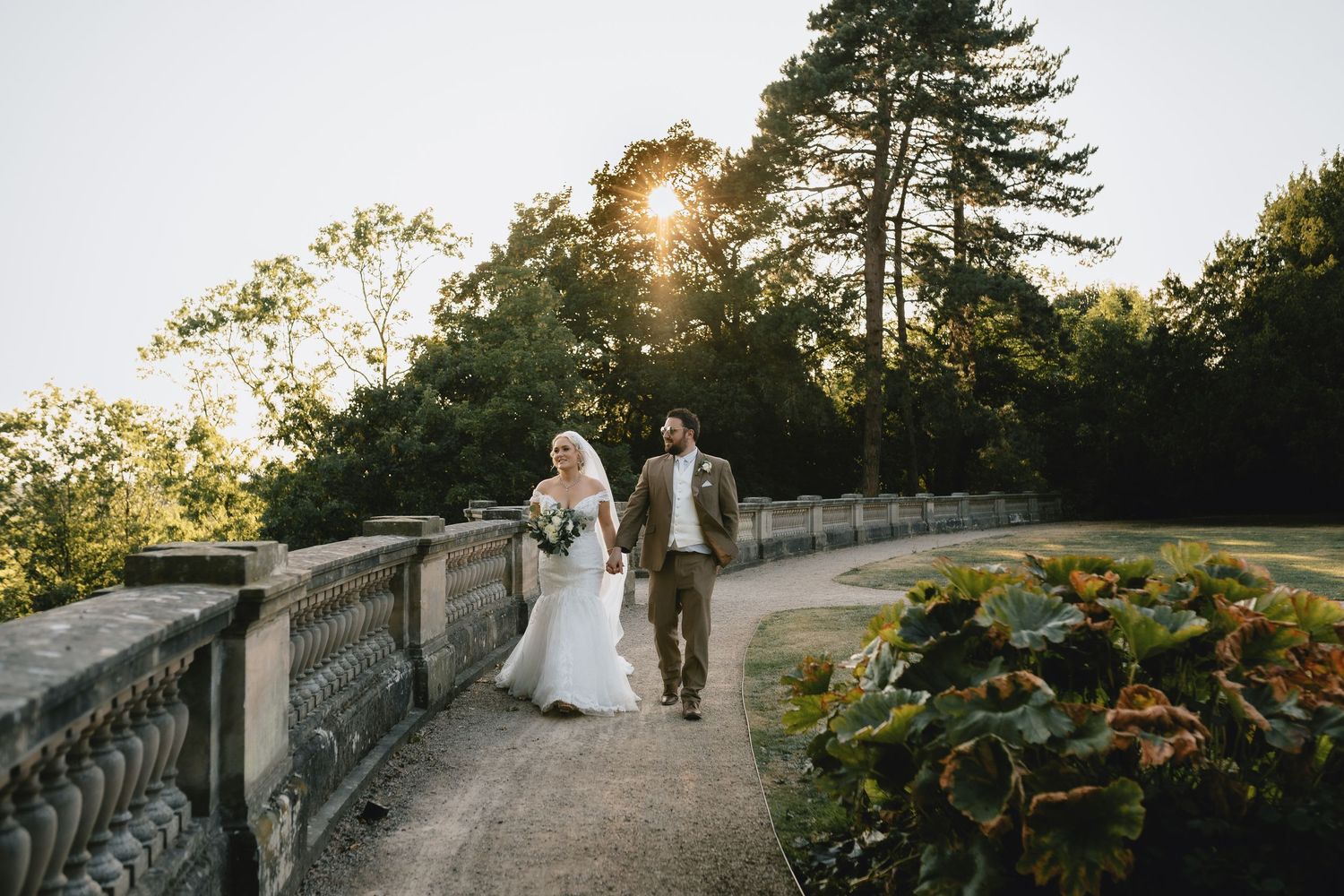 Romantic couple shares tender moment at sunset on stone terrace overlooking scenic garden landscape.