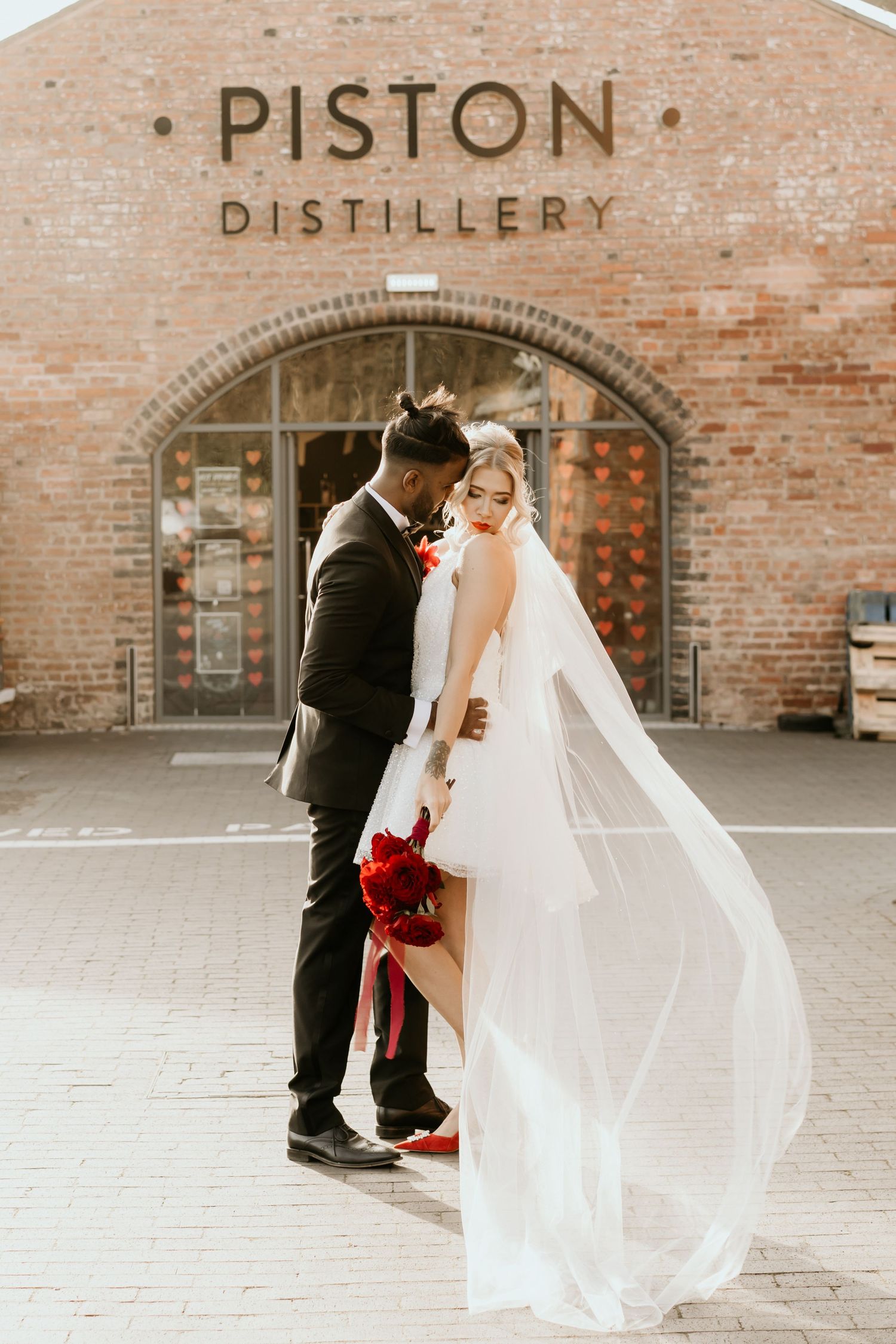 Couple embraces outside brick building with Piston Distillery signage during wedding photoshoot.
