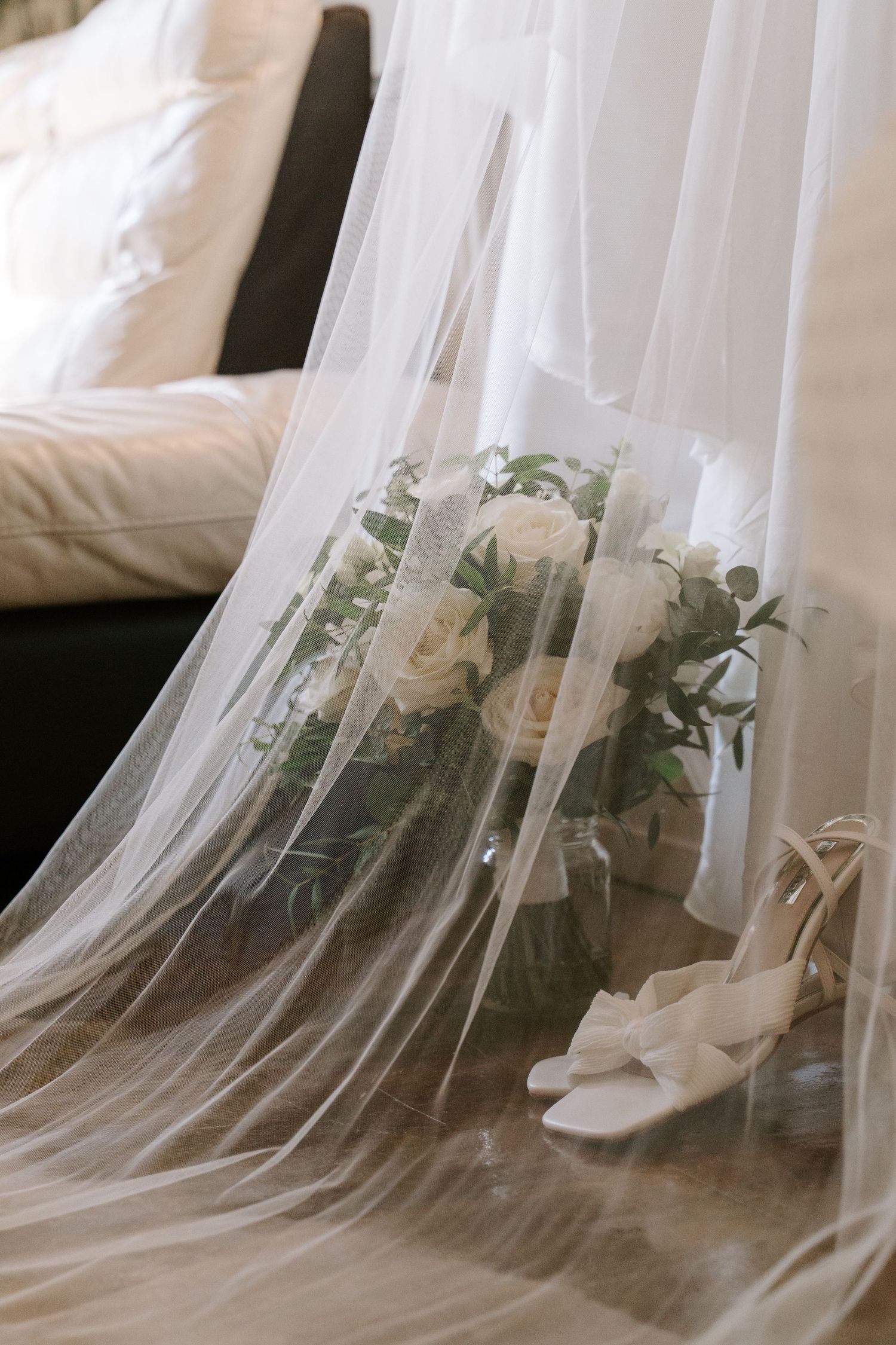 White wedding veil flows elegantly across the floor alongside bridal shoes and delicate floral arrangements.