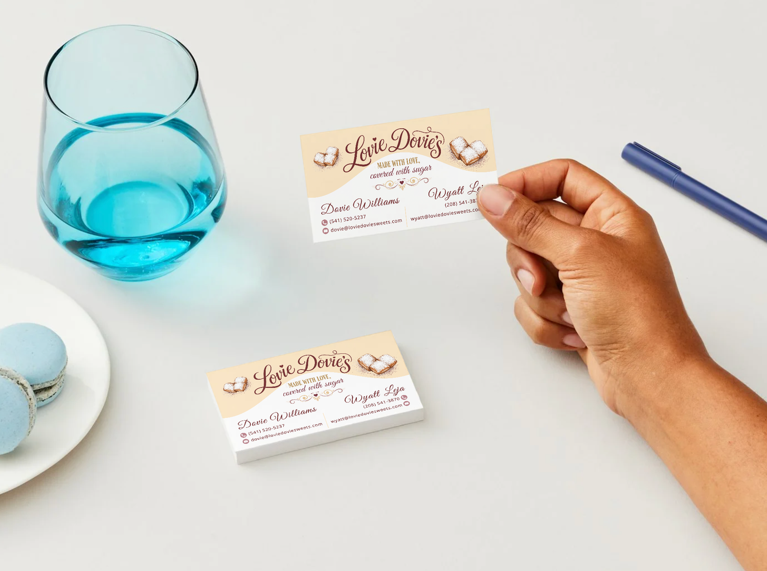 Hand holding a custom business card for Luxe Doves near a blue glass and macarons on a white table.