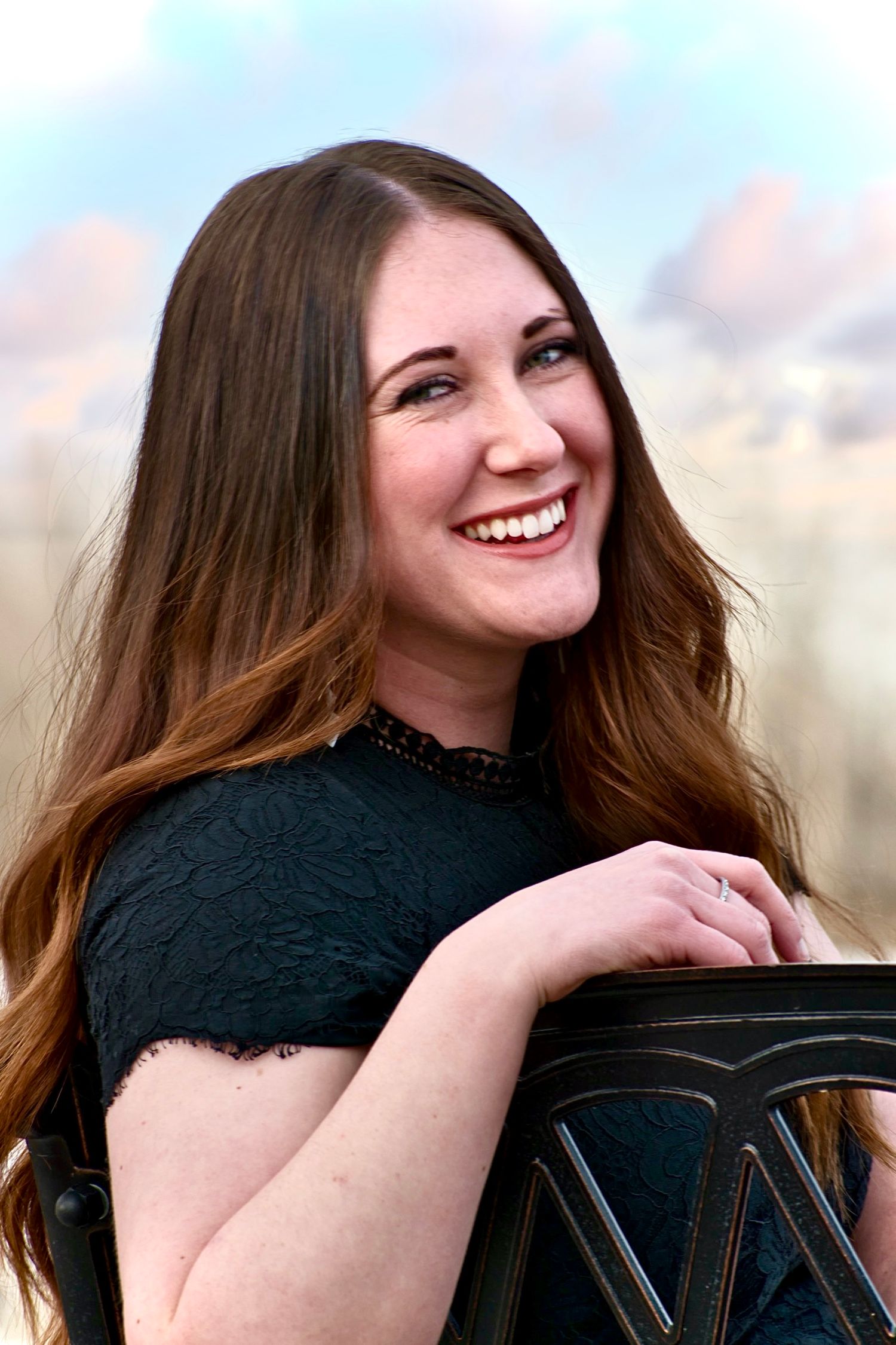 Smiling woman with auburn hair in black lace dress posing outdoors with red rocks.