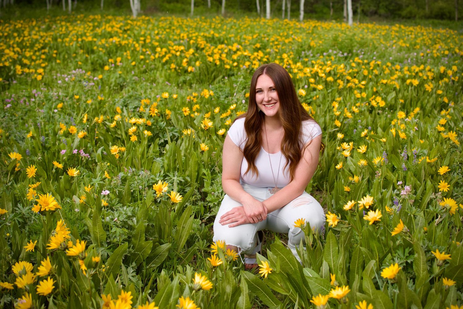 Young woman smiling in a vibrant yellow wildflower meadow on a sunny day.