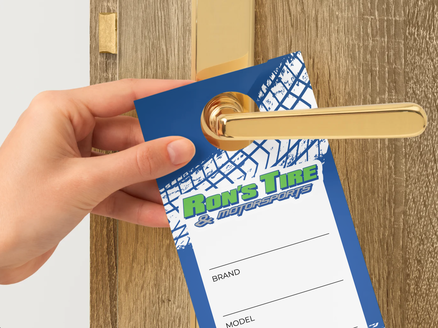 Hand placing a Ron's Tire branded door hanger on a gold door handle, featuring brand and model fields.