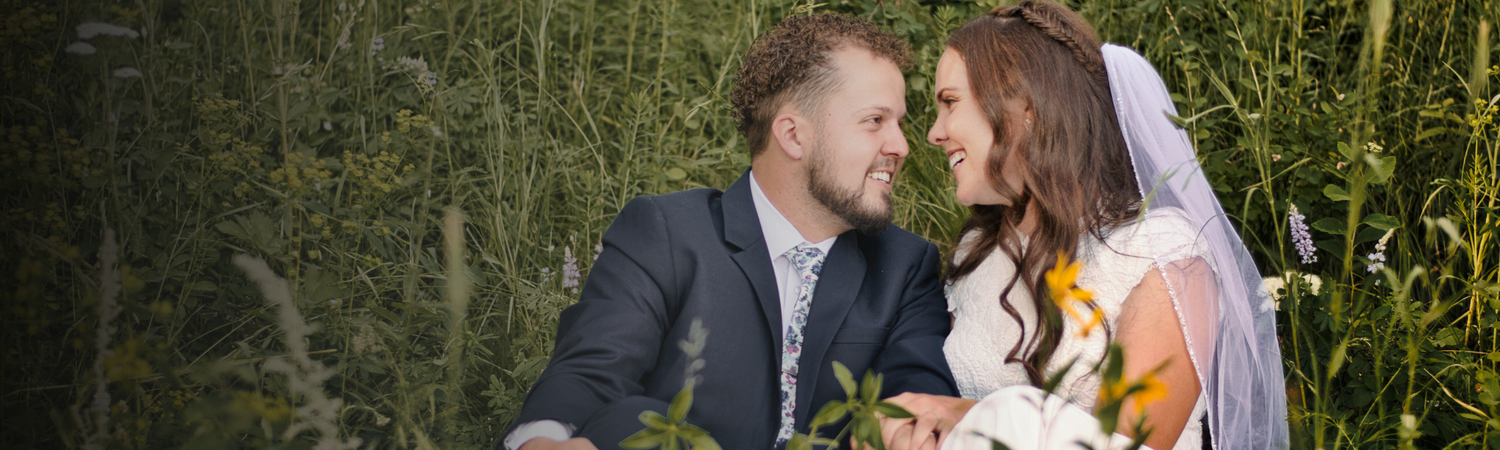 Bride and groom sharing a romantic moment surrounded by tall green grass on their wedding day.