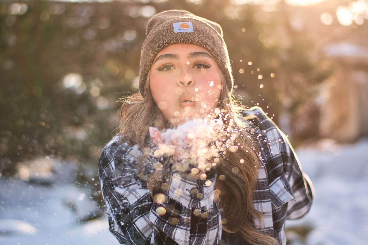 Young woman blowing snow from her hands in a sunny winter forest setting.