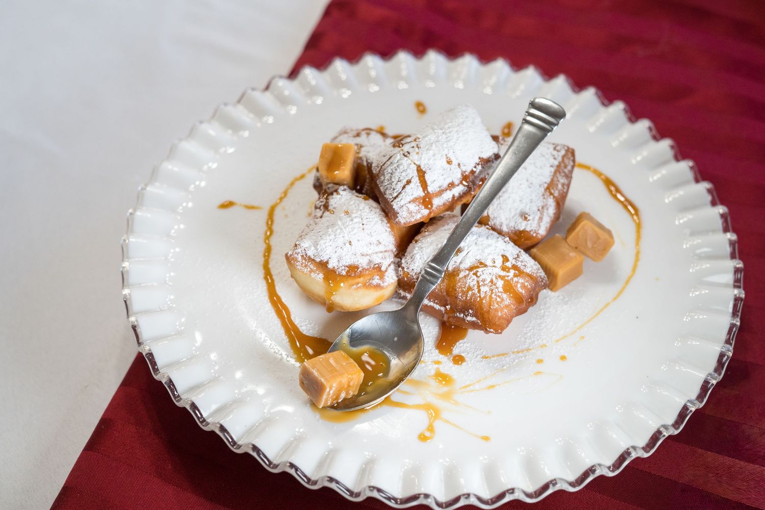 Powdered sugar beignets with caramel sauce and candy pieces on a white decorative plate.