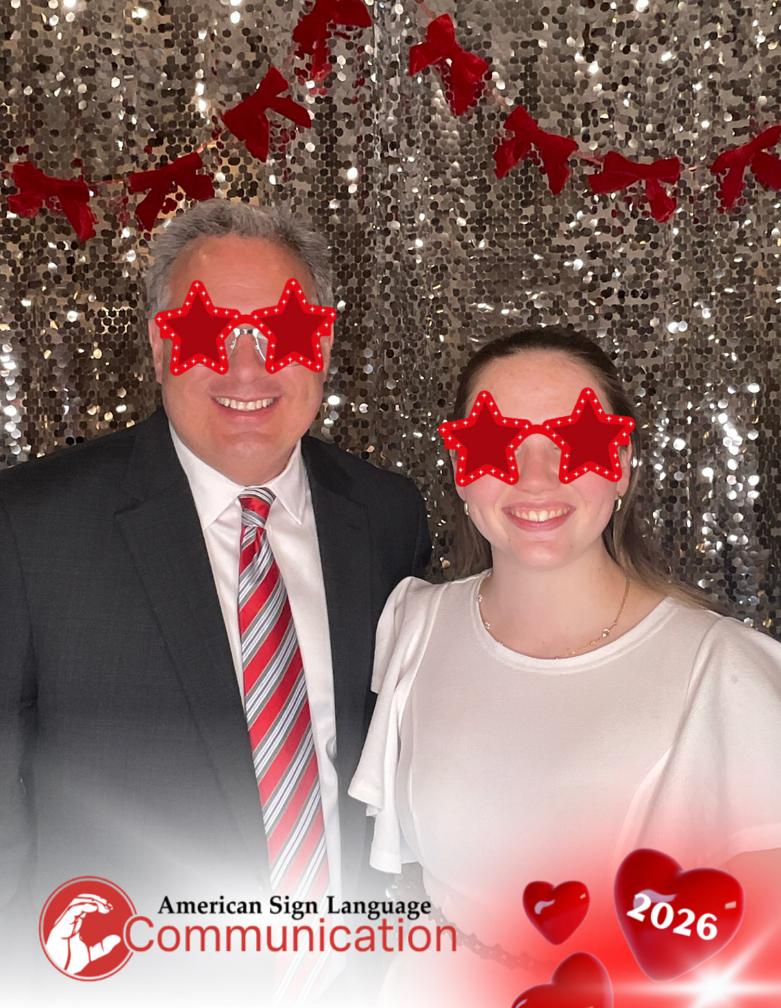 Two people wearing red star-shaped glasses pose at an American Sign Language Communication 2026 event photo booth.