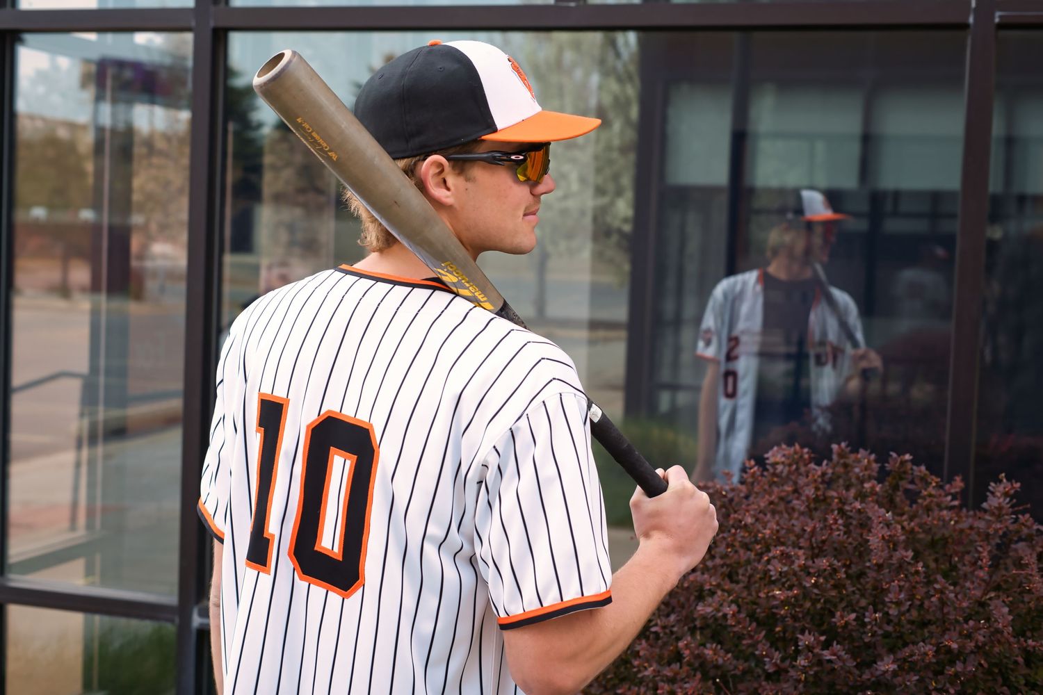 Young baseball player in number 10 pinstripe uniform holding a bat over his shoulder outside a building.