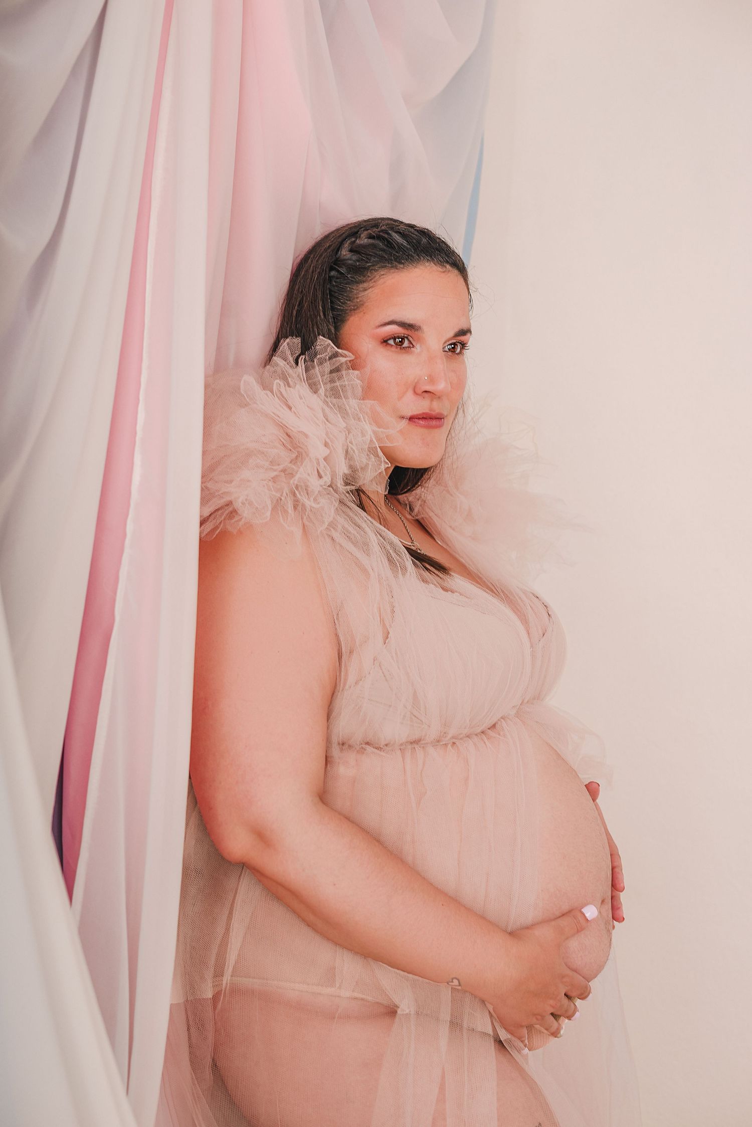 Maternity photoshoot featuring soft pink tulle fabric and ethereal lighting in a series of connected poses.
