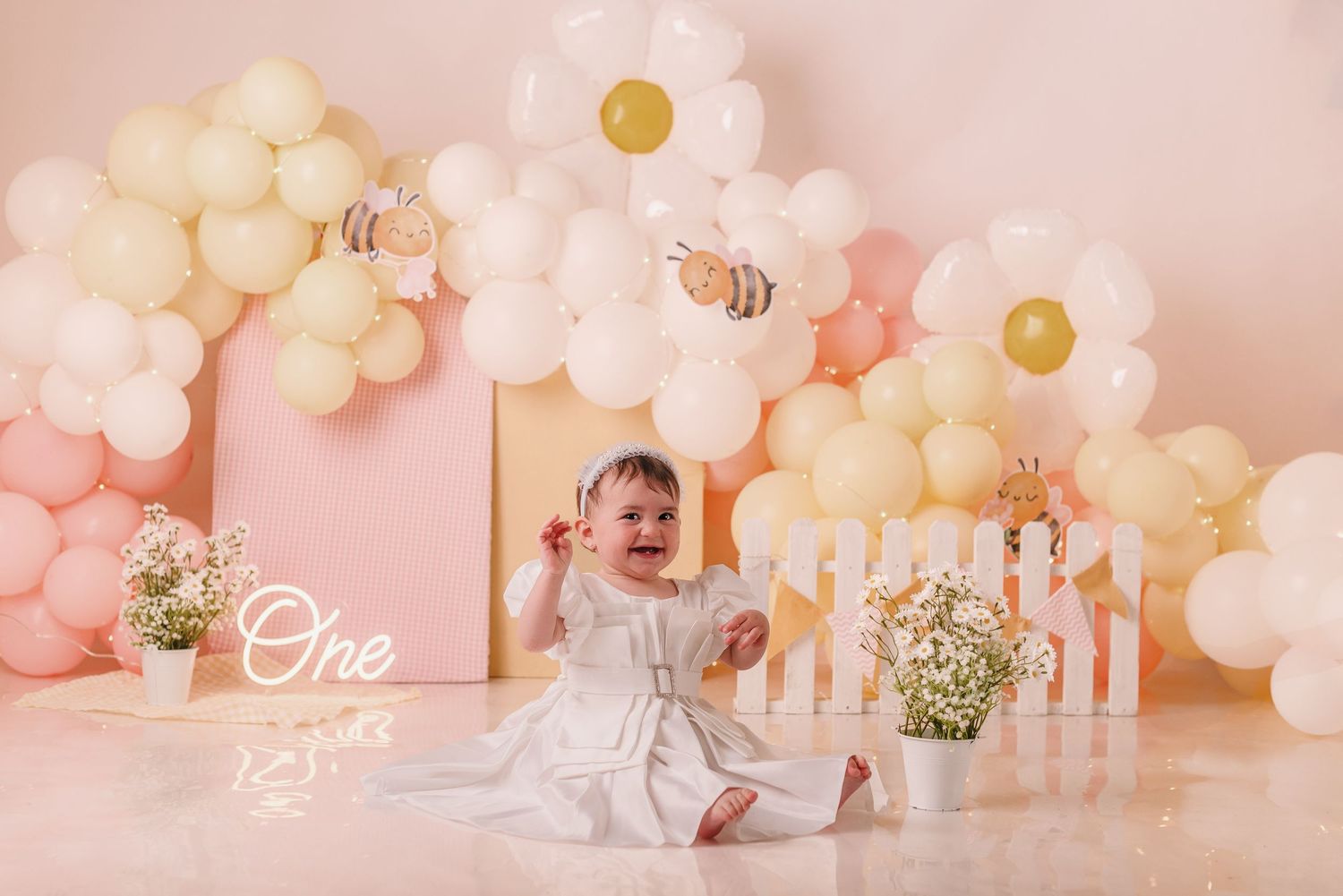 First birthday party setup with elegant white and gold balloon garland and floral decorations.