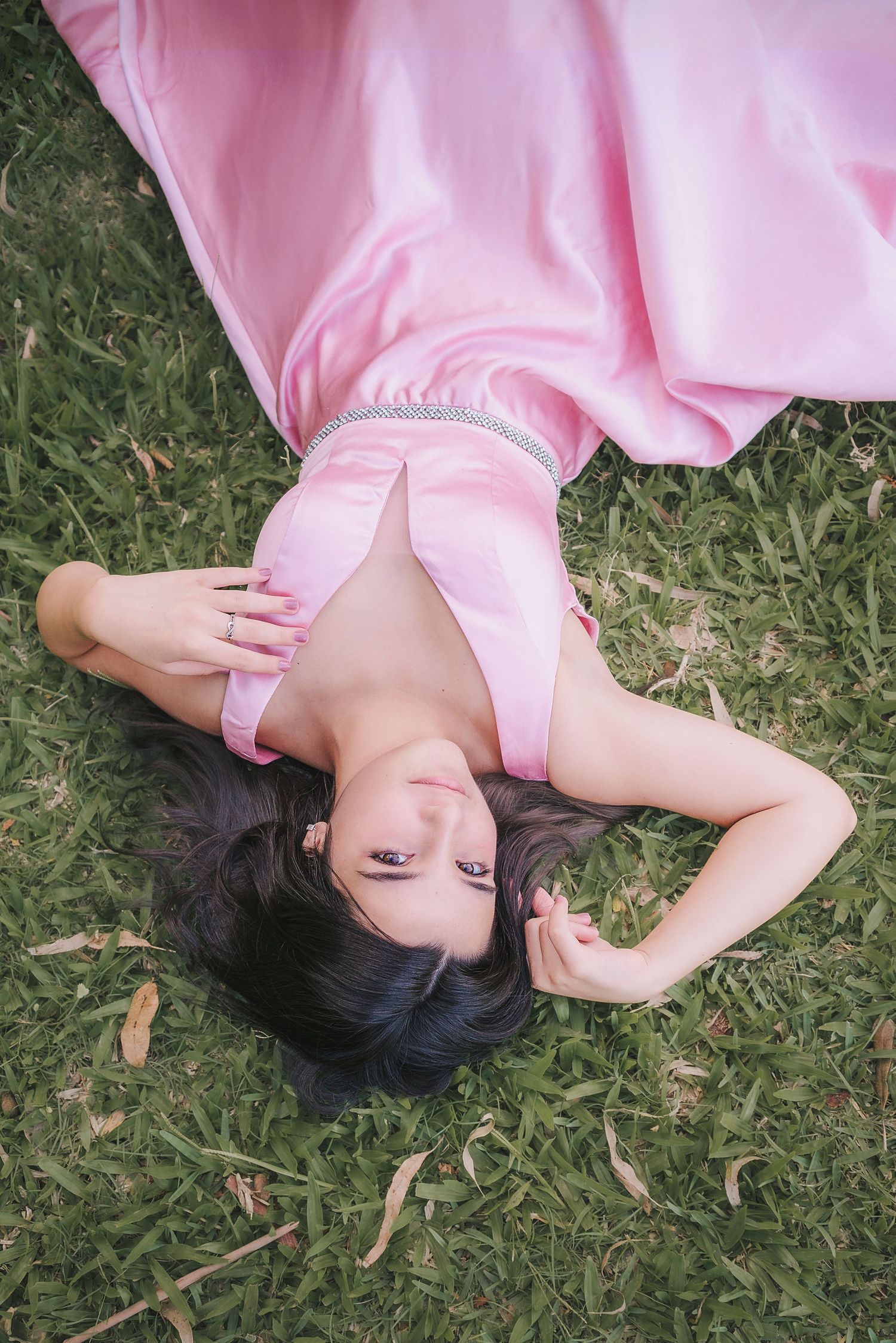 Person in pink satin dress lying on grass in a dreamy pose with scattered leaves around them.