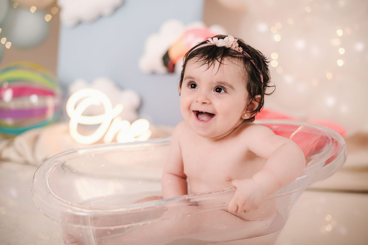 A happy baby sits in a bathtub with soft lighting and bokeh effects in the background.