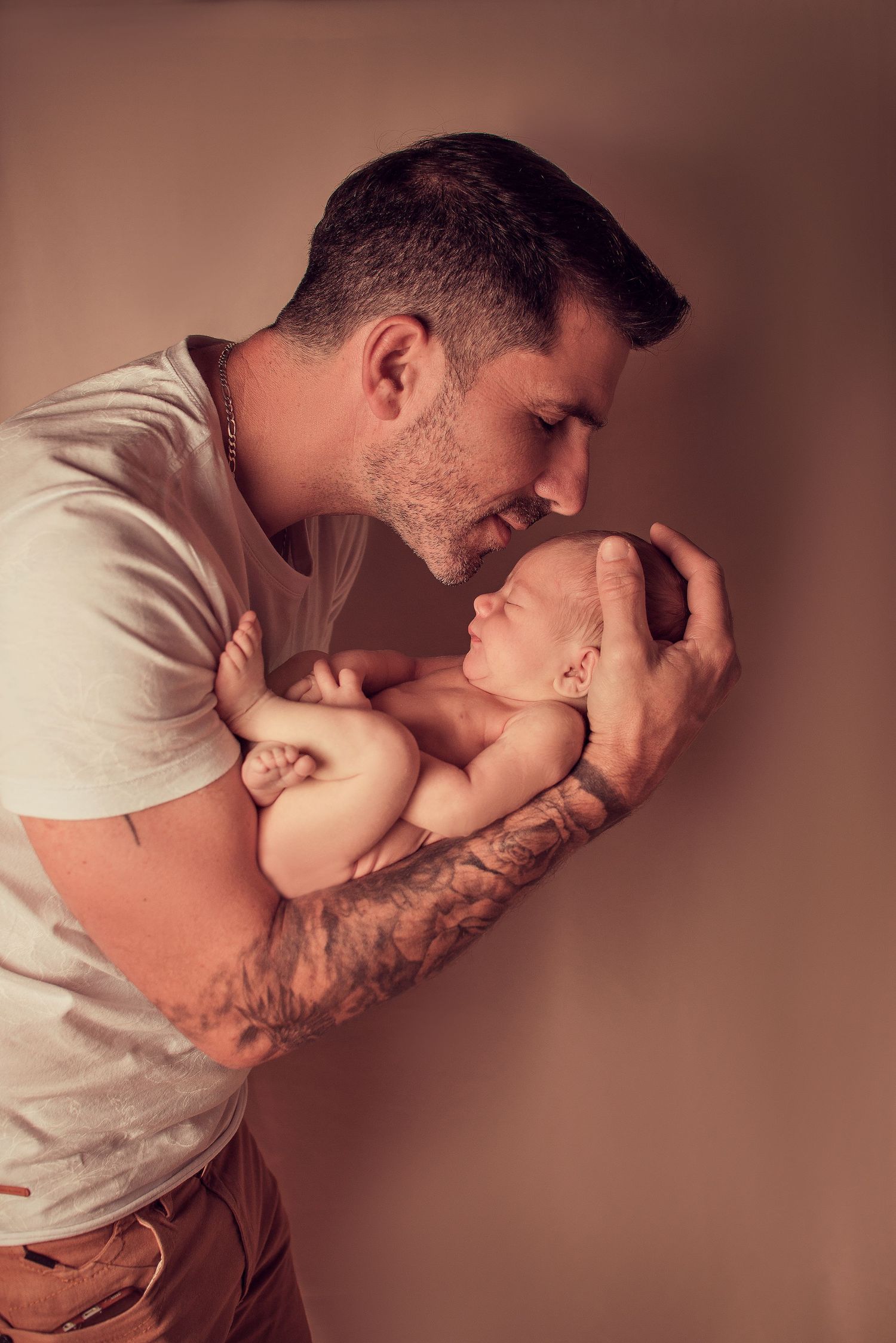 A tender moment between parent and newborn baby in soft brown lighting shows gentle nurturing and bonding.
