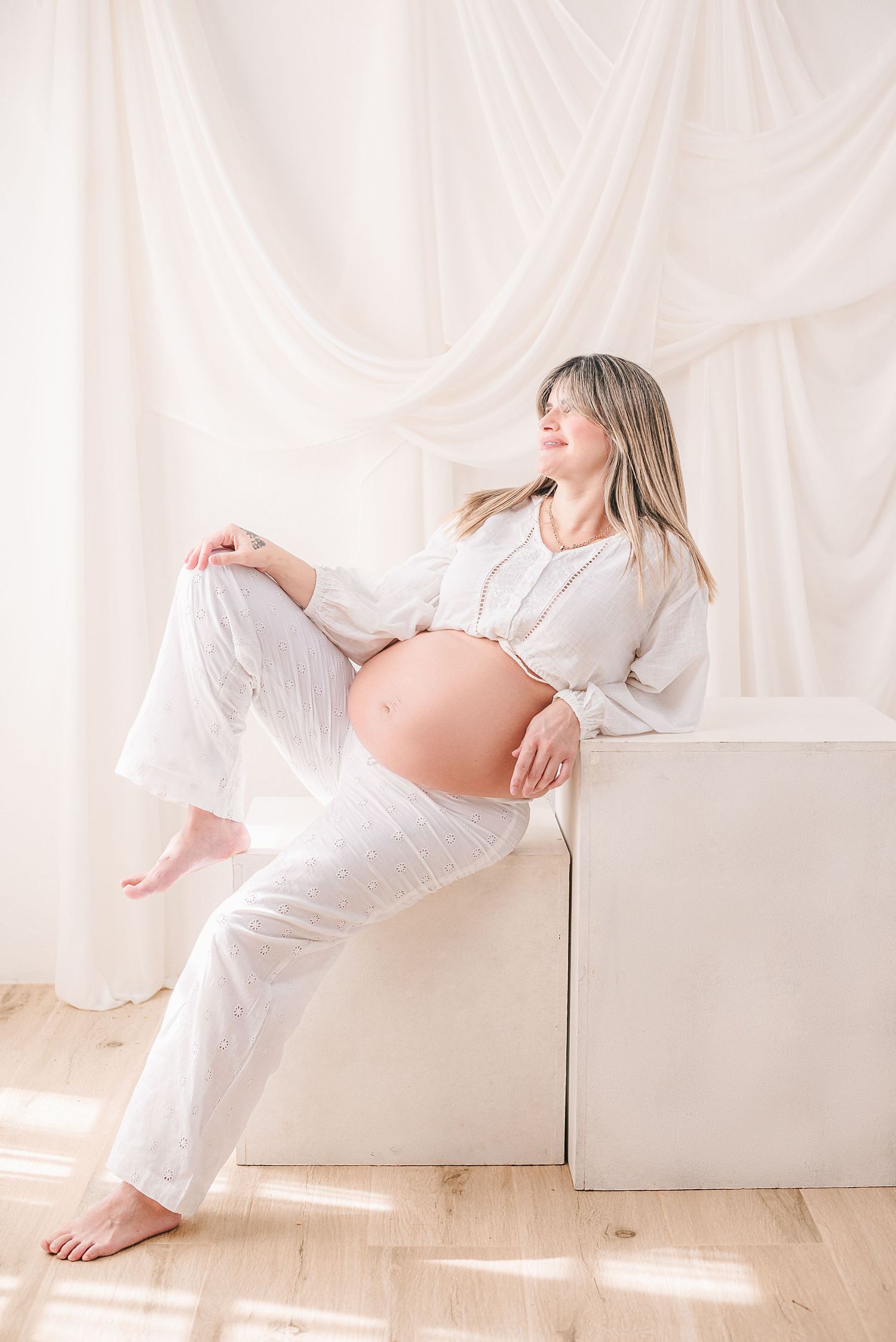 Elegant maternity photos in white featuring poses on a light backdrop.