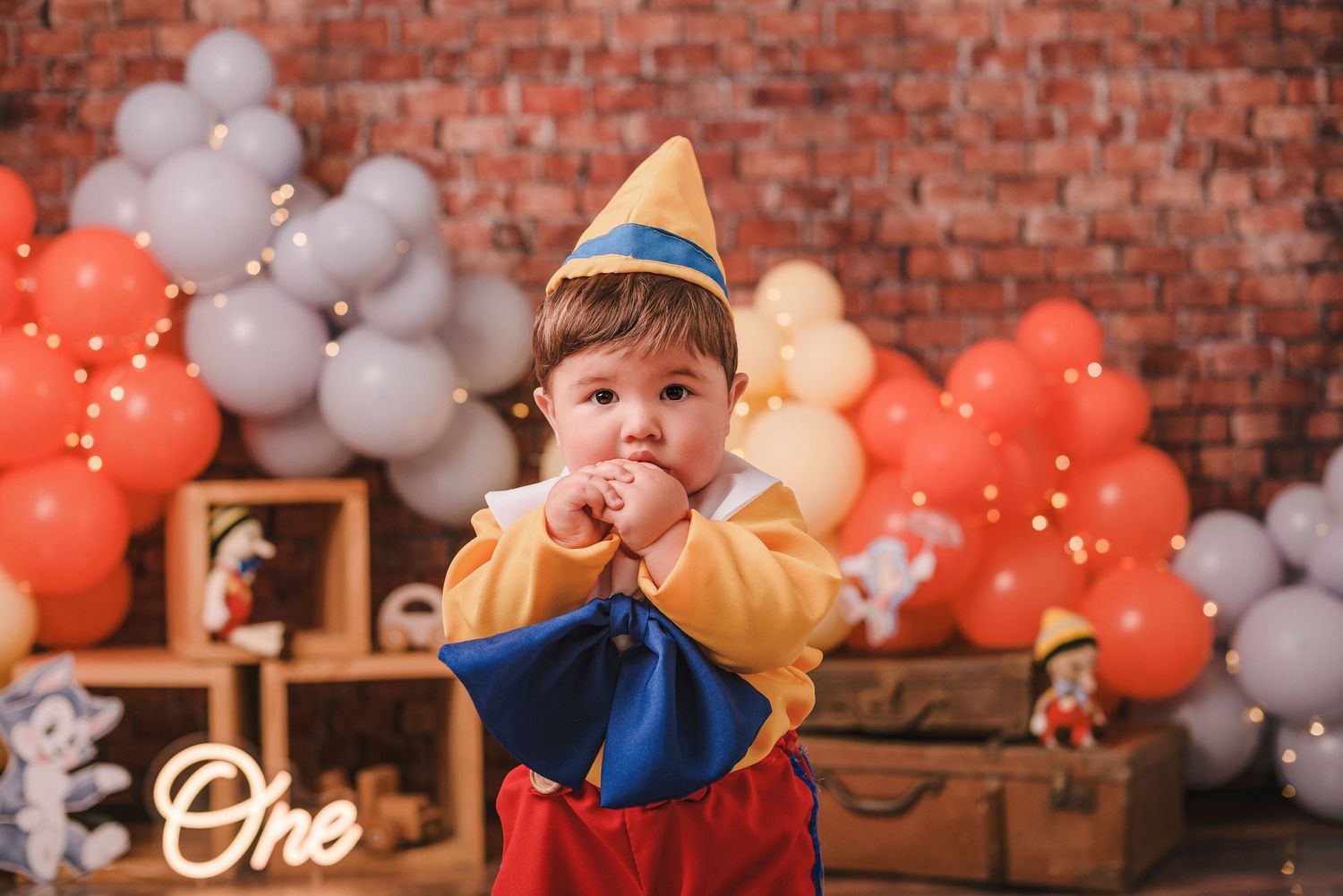 Birthday party decorations featuring orange and gray balloons against a rustic brick wall backdrop.