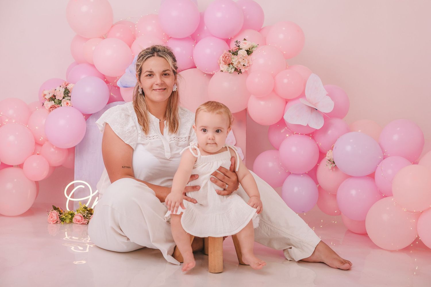Sweet baby photography session with pink and purple balloon arch backdrop and floral decorations.