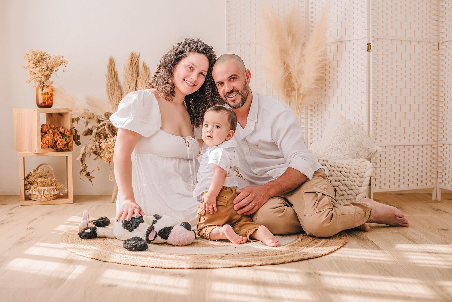 A family sits together on a round rug in a cozy room decorated with pampas grass and warm lighting.