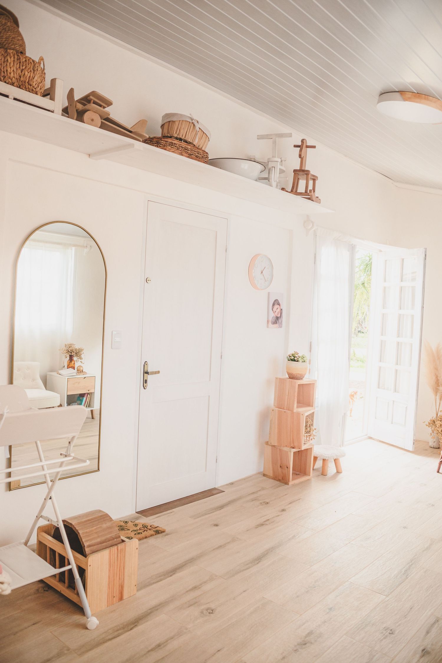 Bright minimalist photography studio with white walls, wooden floor, and vintage baskets on shelf.
