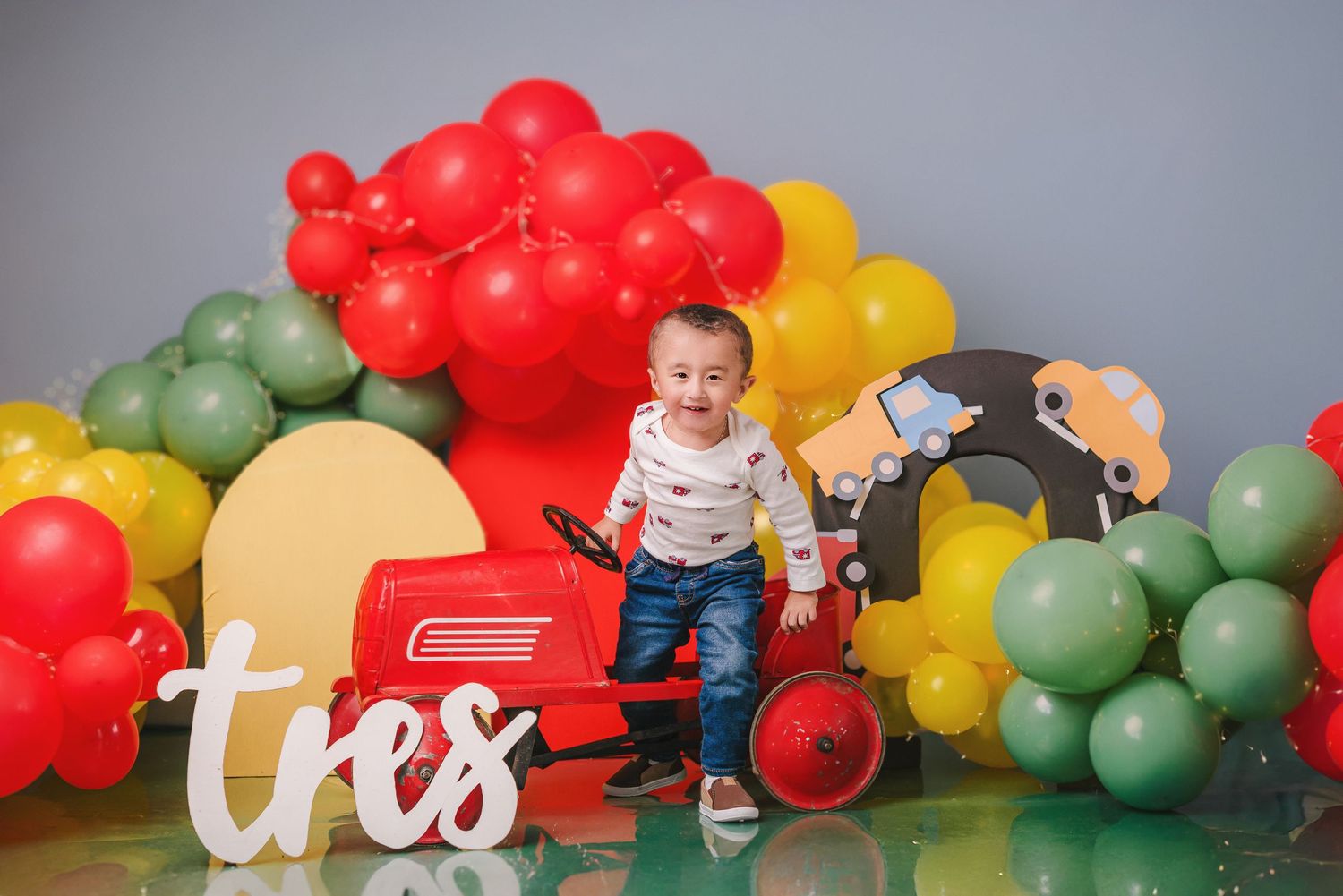Colorful balloon arch installation with red, yellow, and green balloons against a gray wall for party decoration.