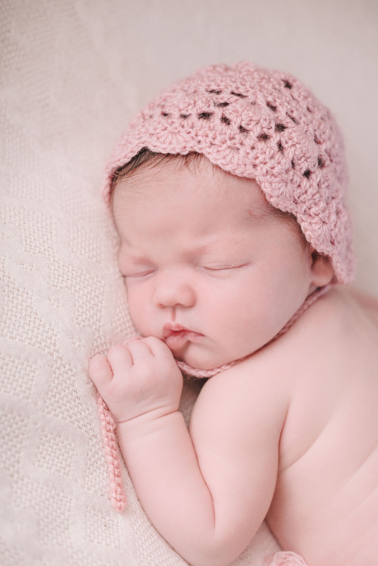 Sweet newborn portrait with pink lace bonnet against white textured background.