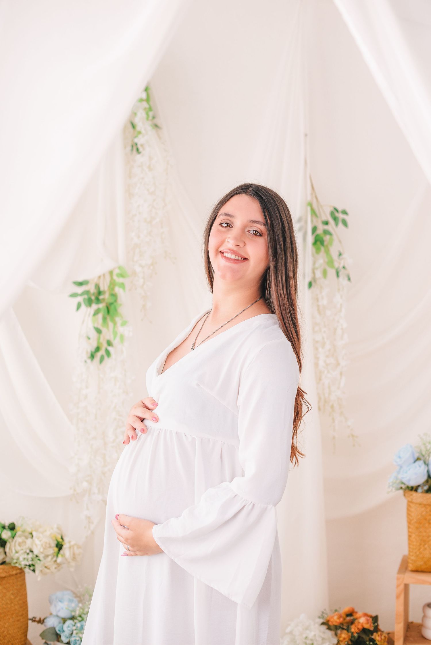 A person in a flowing white dress poses gracefully against a light backdrop with delicate greenery and floral accents.