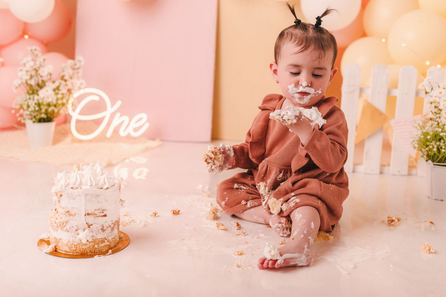 A collage of pink-tinted cake smash photos showing a baby eating and playing with birthday cake.