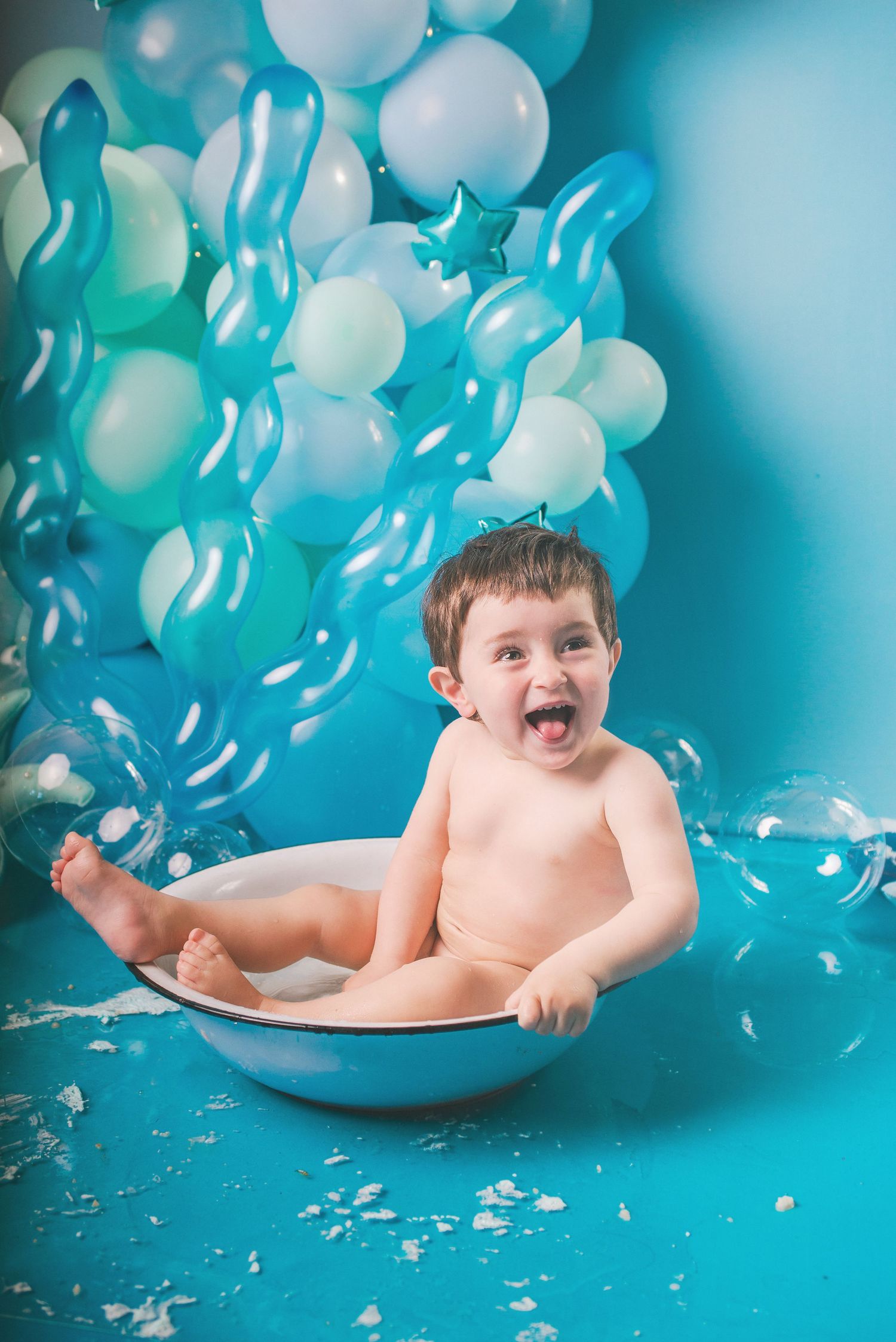 Joyful bath time moment with bubbles and balloons against turquoise background in whimsical portrait setting.