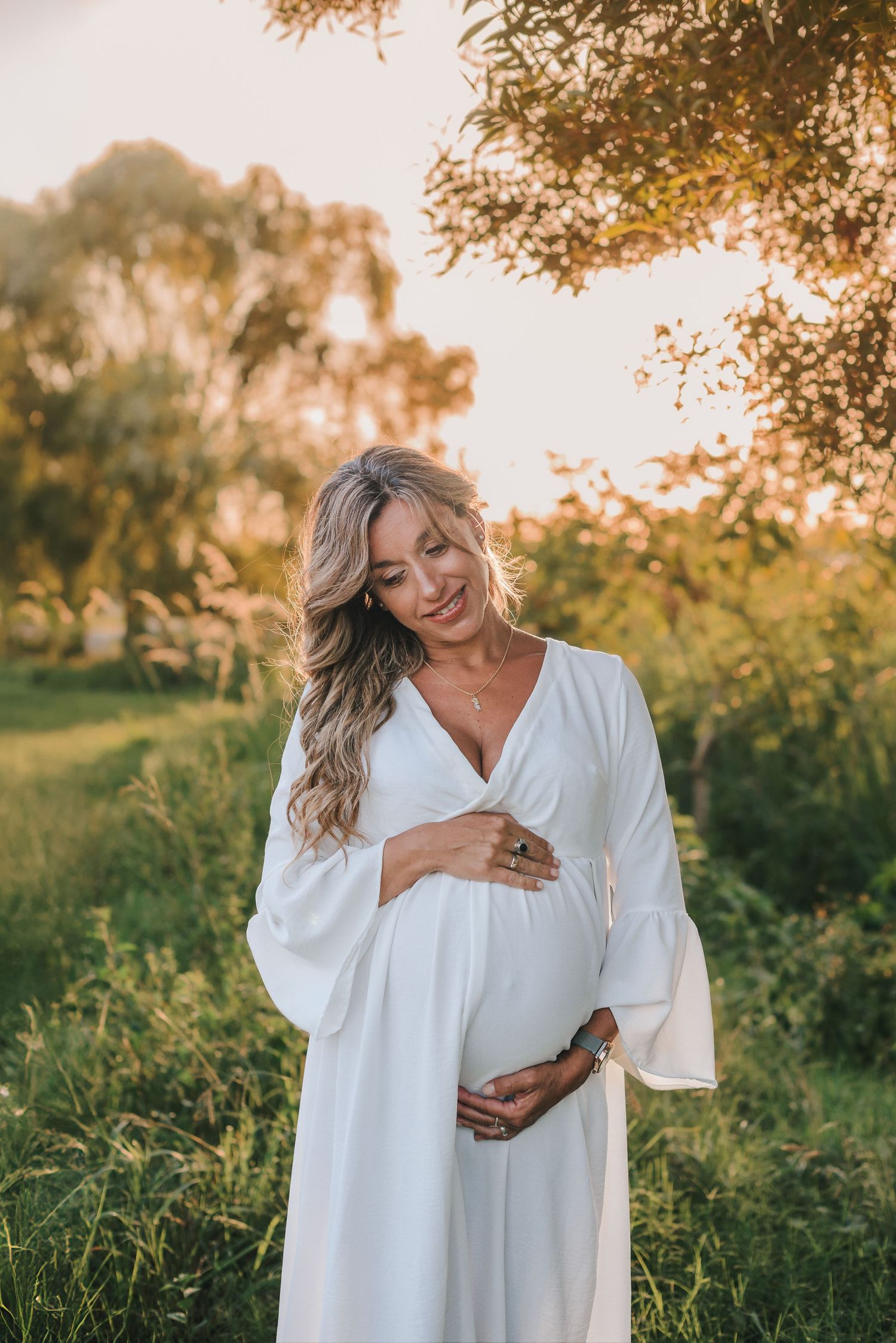 Woman in white dress laughing joyfully in outdoor garden setting at sunset.