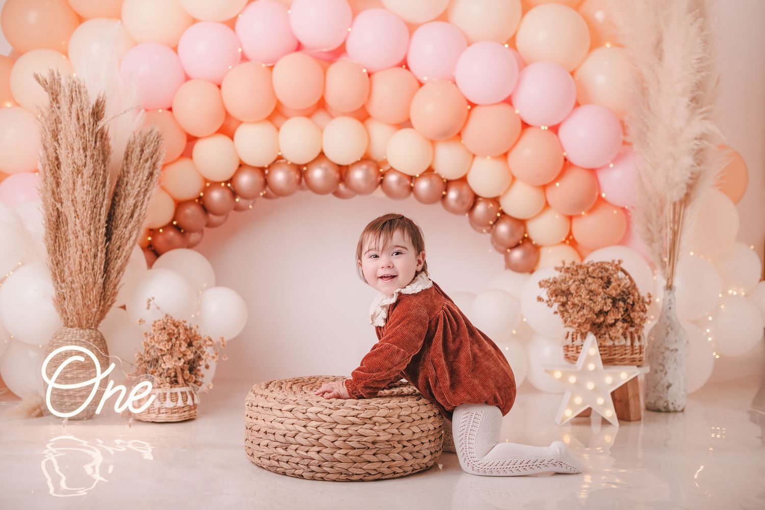 Elegant birthday setup with peach balloon arch, pampas grass, and neutral toned decorations.