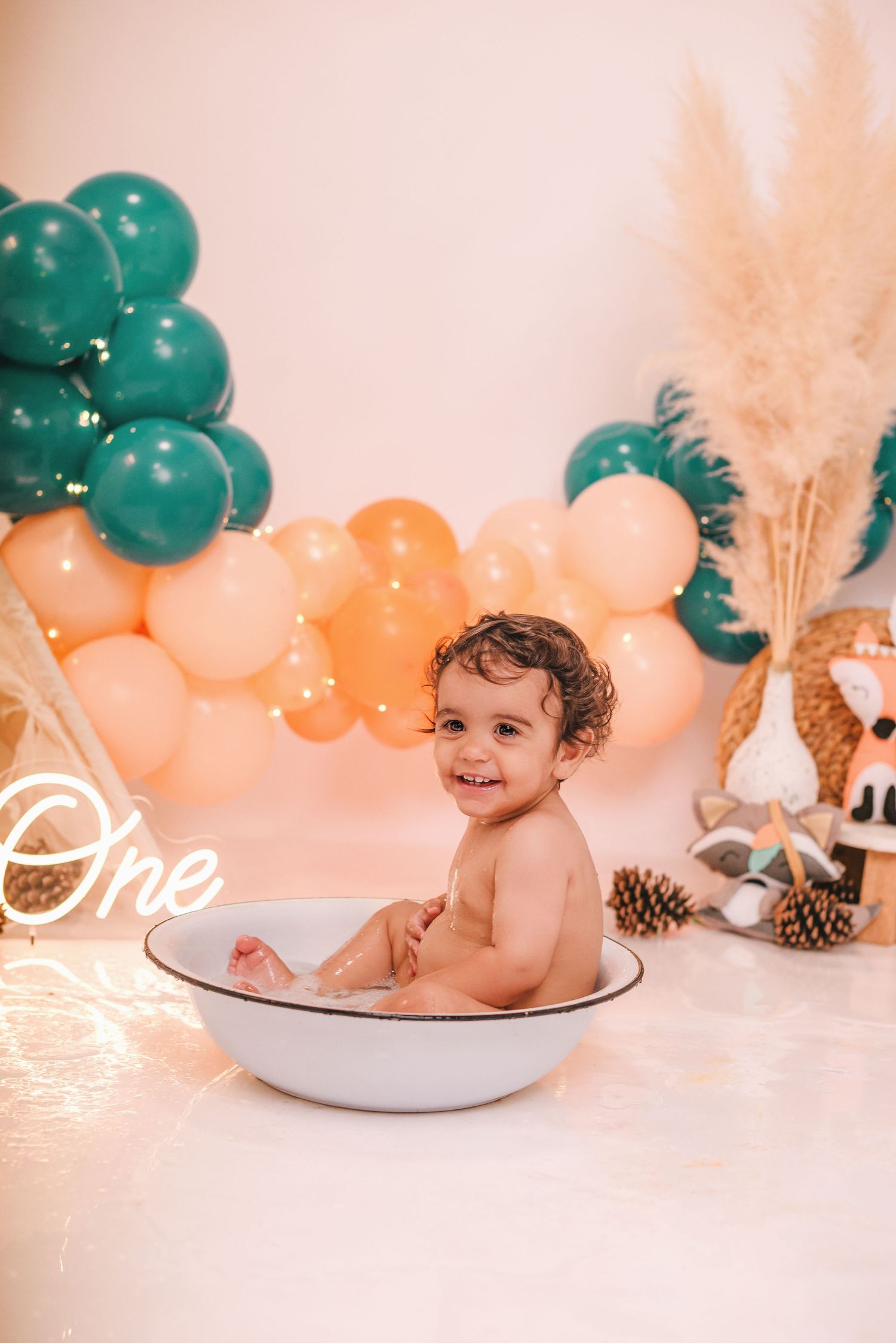 A baby's cake smash photo session with peach and teal balloon decorations and pinecone accents.