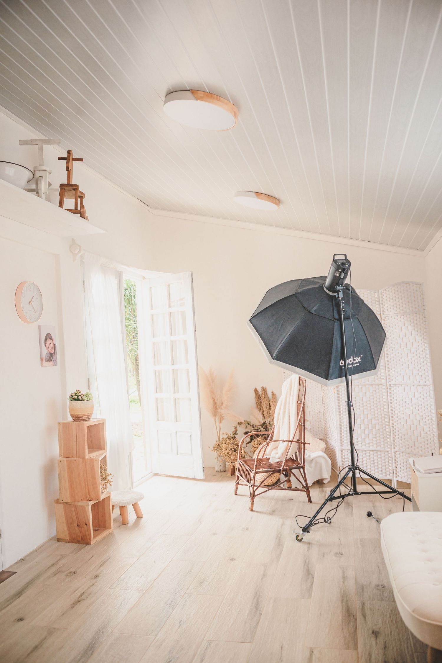 Photography studio setup with black softbox light and rattan chair against white walls.
