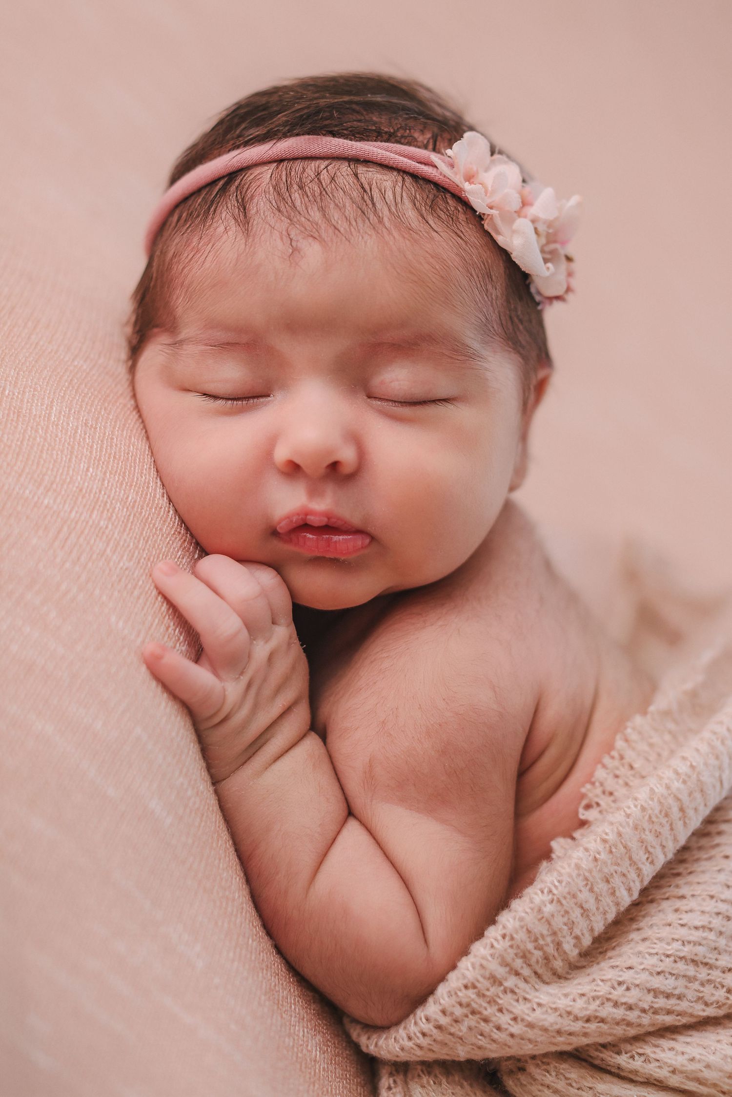 Closeup newborn photography with soft pink backdrop and delicate headband.