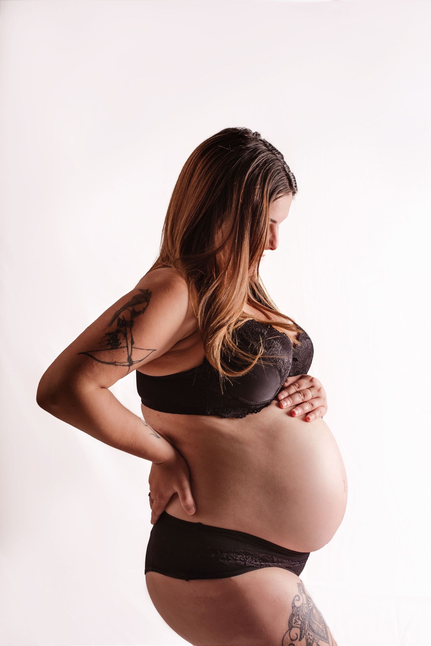 Artistic black and white maternity photography series showing pregnant woman in dark bra against light background.