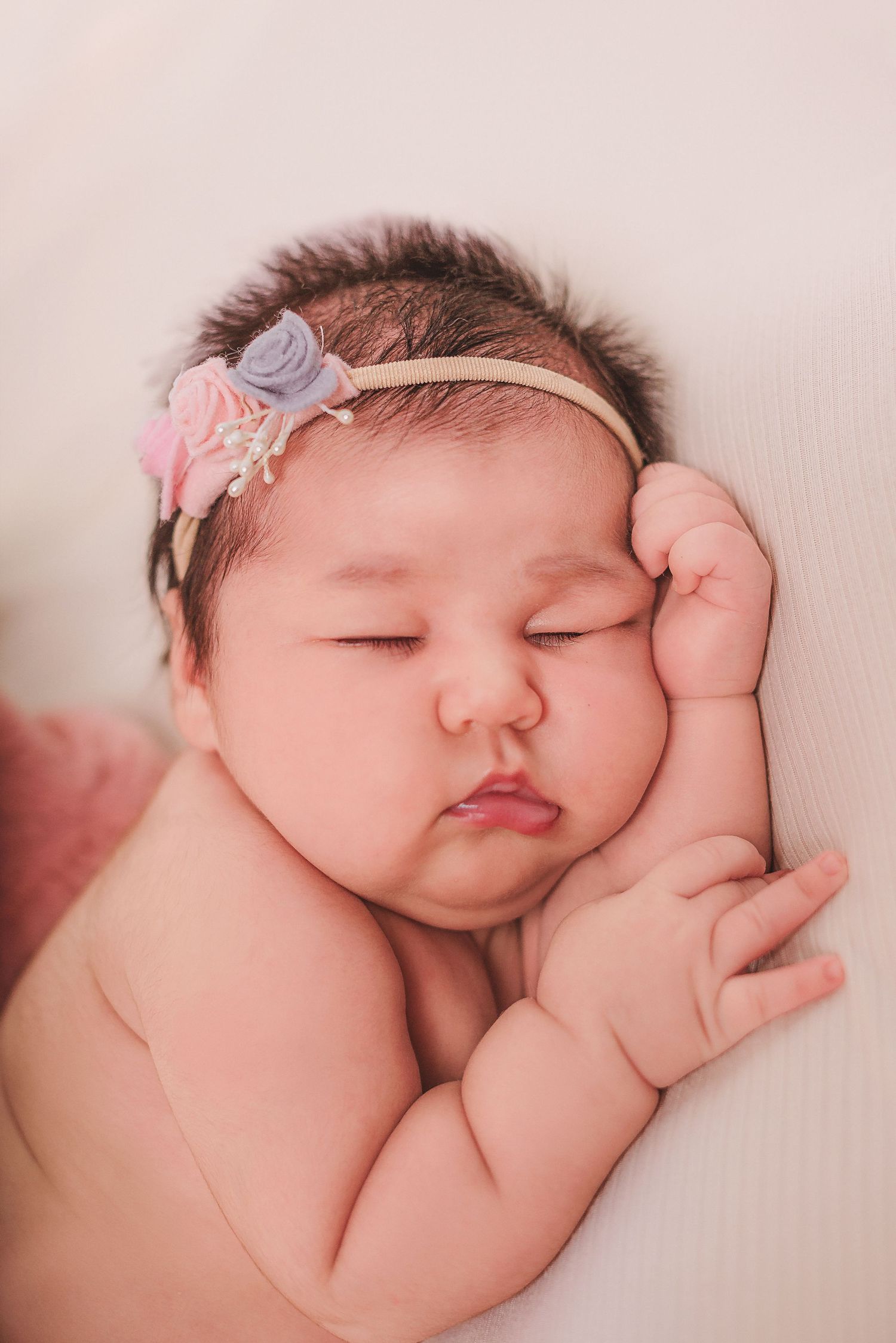 A sleeping newborn baby in pink tones curled up peacefully during a professional photography session.