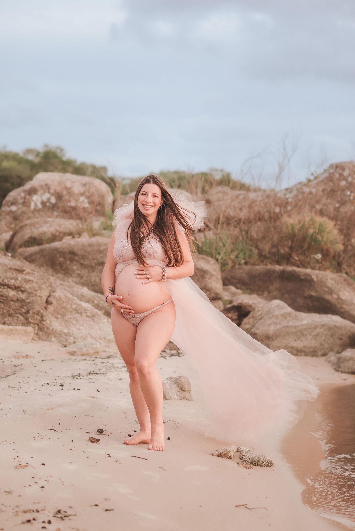 Maternity beach photo with flowing dress and natural coastal backdrop.