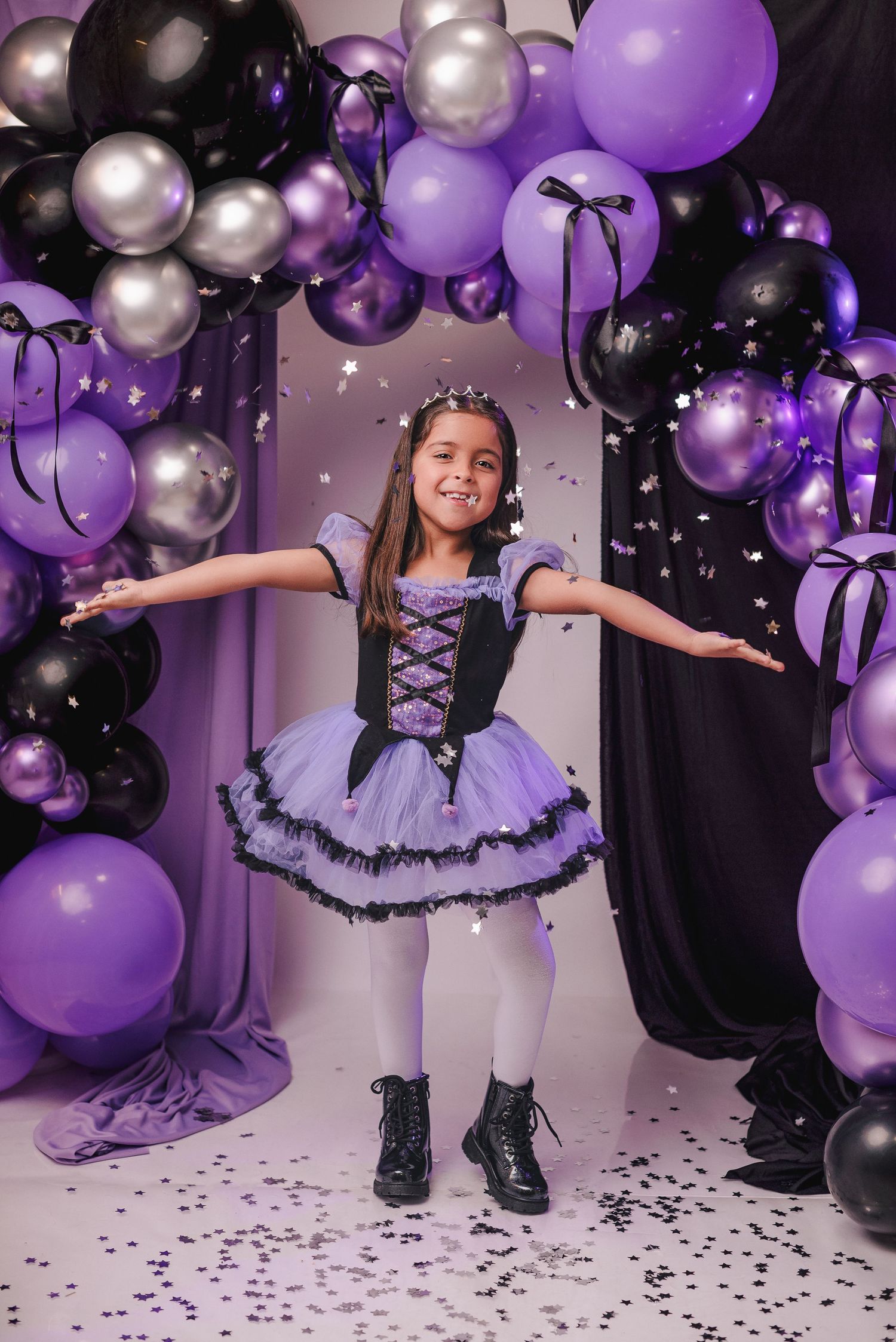Party scene with purple and silver balloons against a white backdrop with black confetti scattered on the floor.