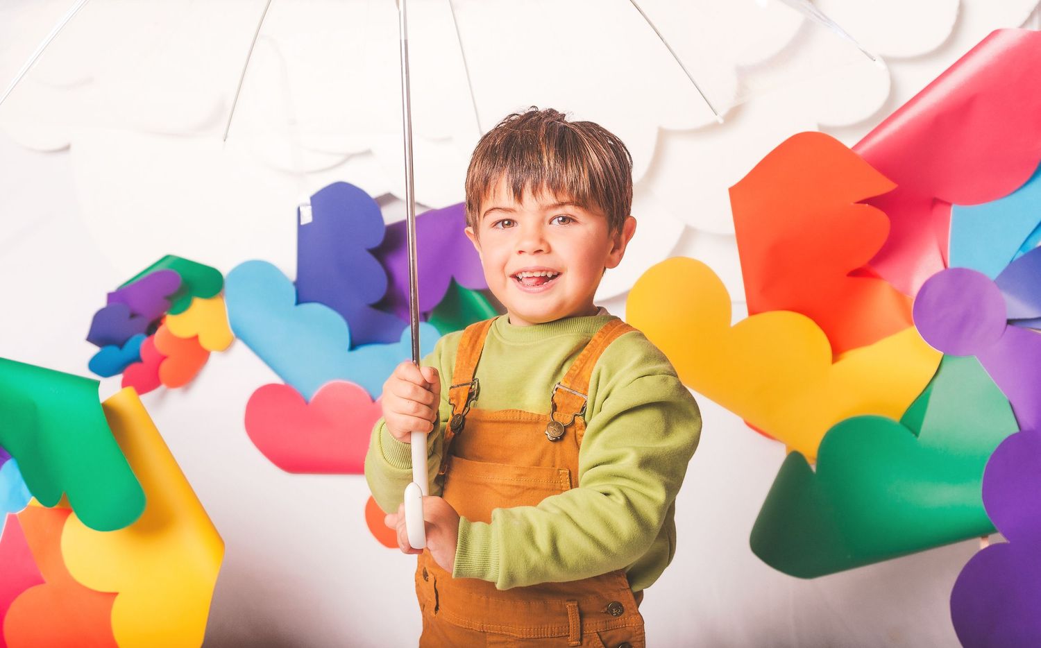 Happy young boy holding umbrella surrounded by colorful paper hearts on white background.