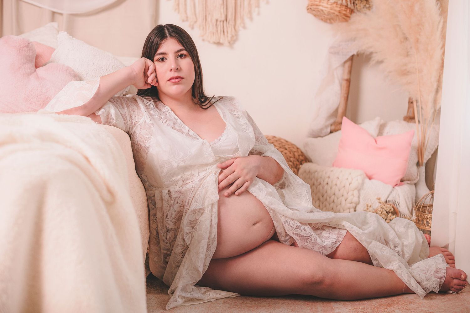Maternity boudoir photo with soft pink decor and lace details in romantic setting.