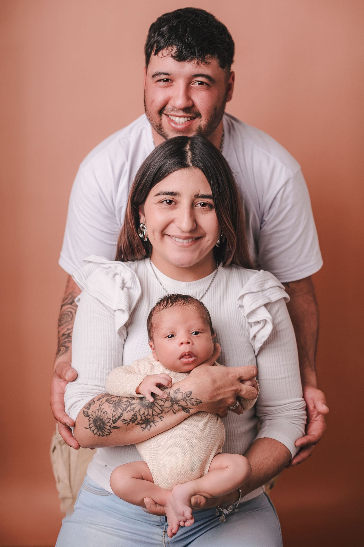 A series of intimate family portrait photos showing parents with their baby against a warm pink-toned background.