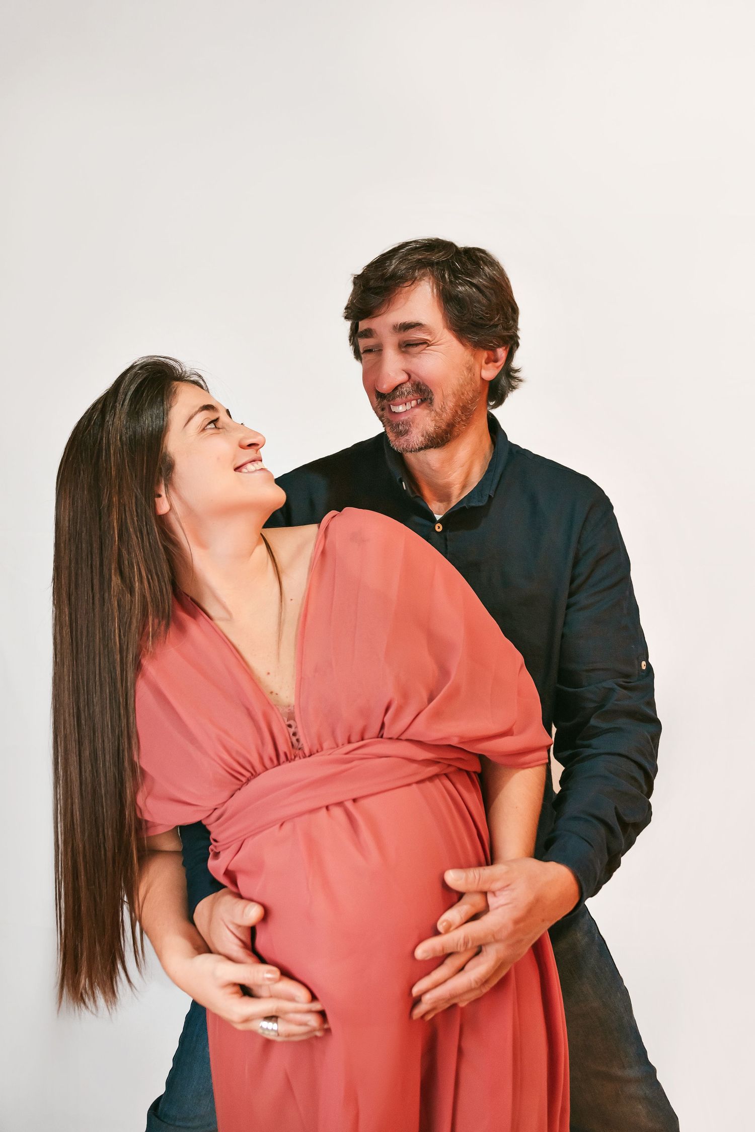 A couple shares a joyful moment together, with one wearing a coral dress and the other in dark clothing.