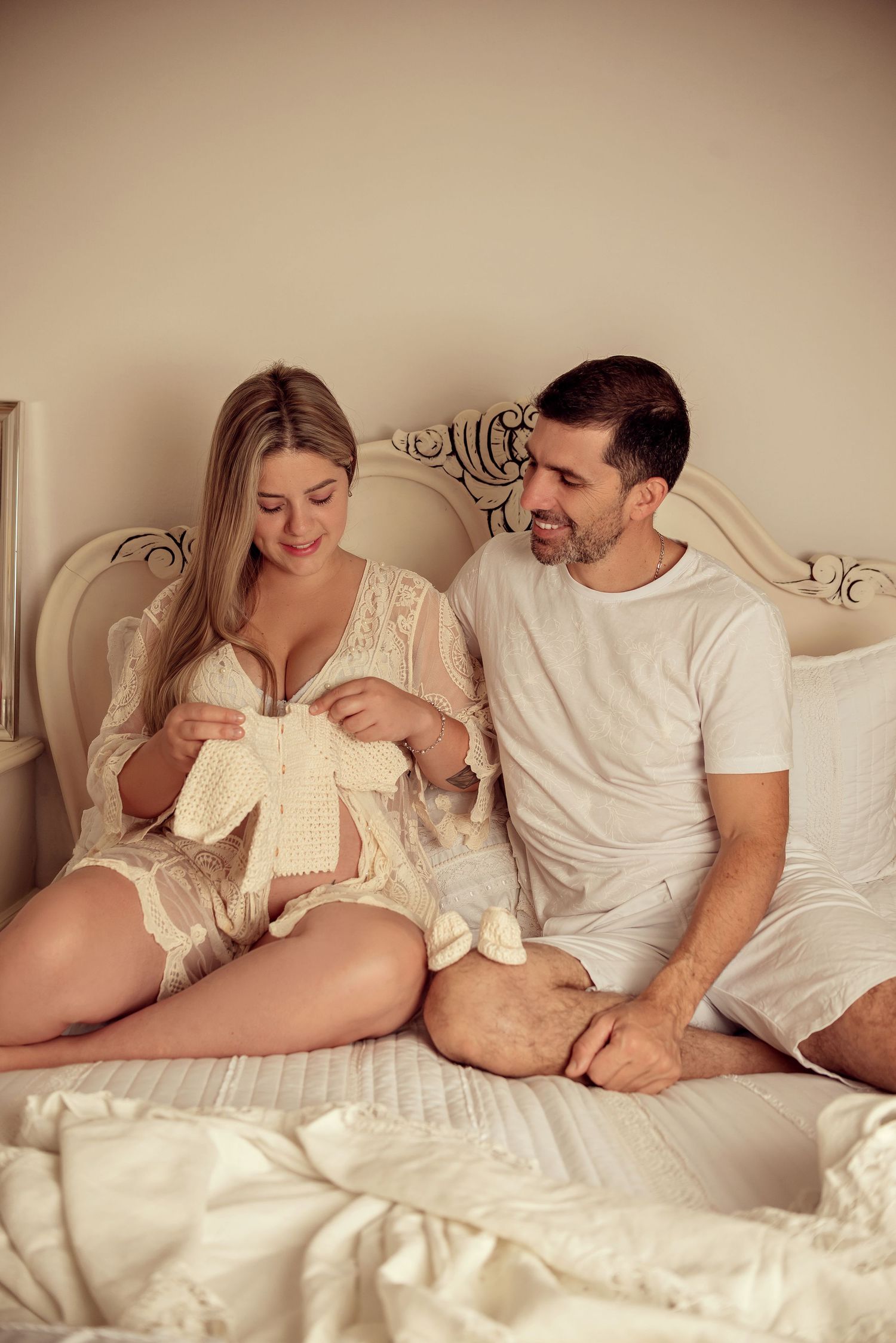 Couple sharing an intimate moment while lying together in bed with white linens and decor.
