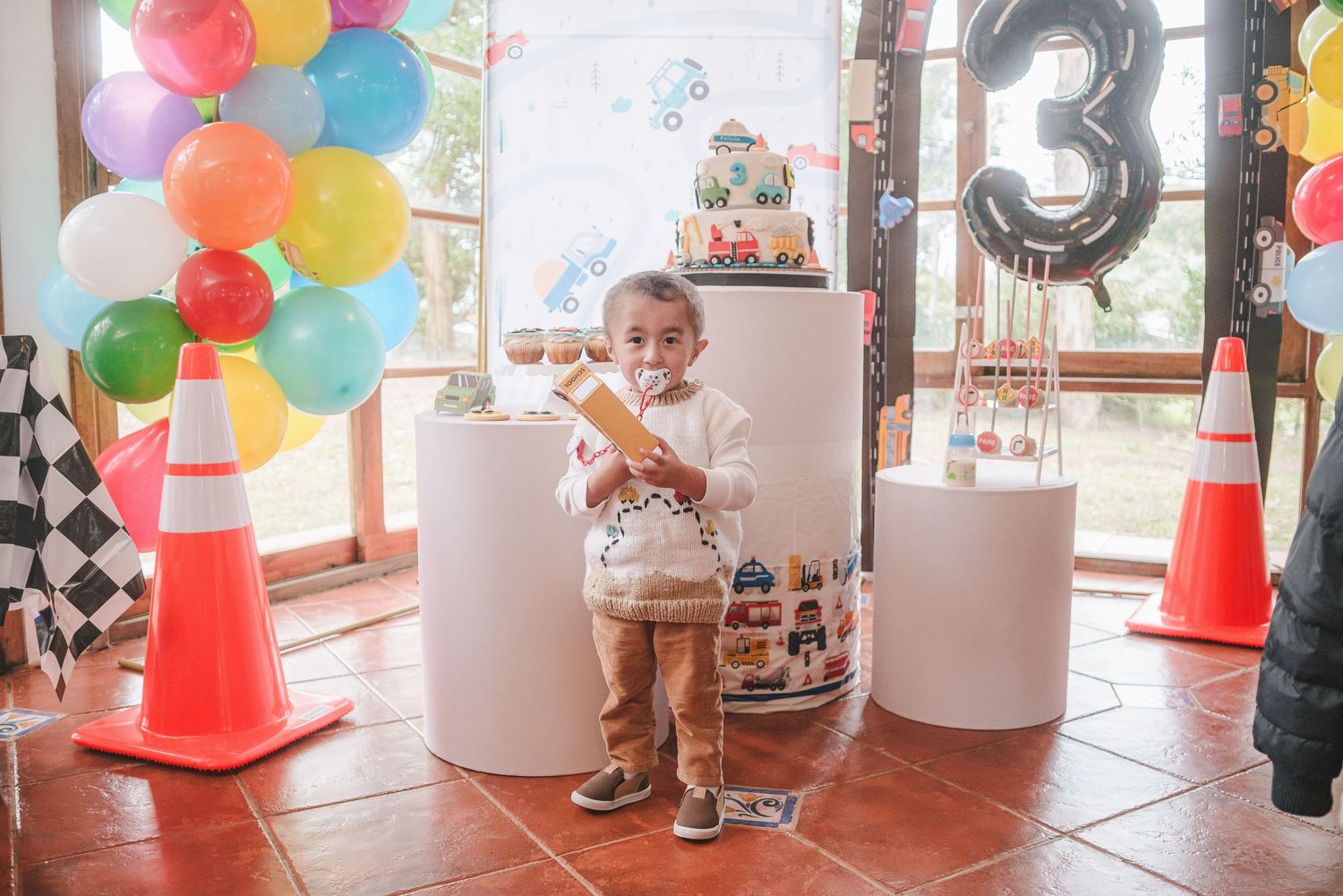 Birthday party setup with colorful balloon arch, decorative pedestals, orange traffic cones, and a large number 13 balloon.