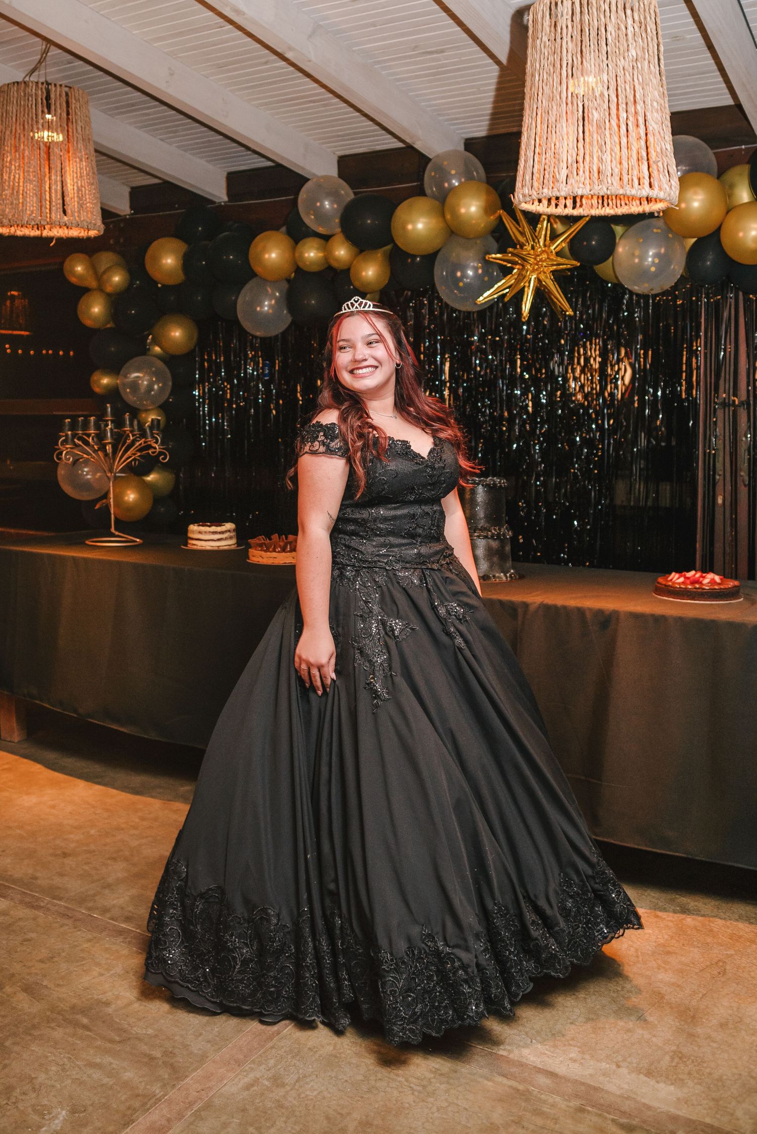 A black formal ball gown with intricate details sparkles under warm lighting at an elegant party venue.