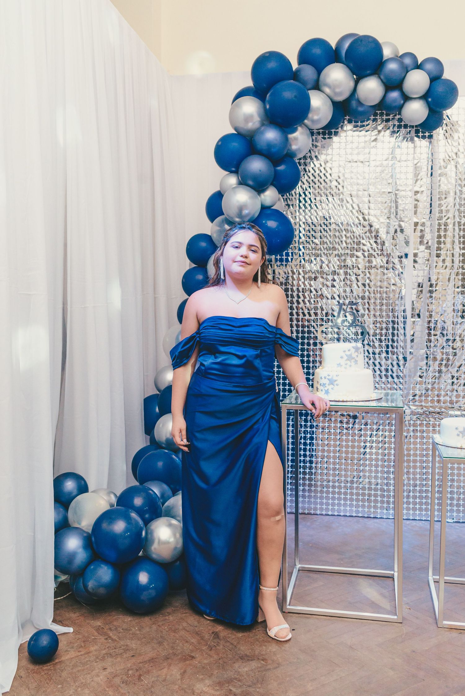 A glamorous event setup featuring a silver sequin backdrop with blue and silver balloon garland decorations.